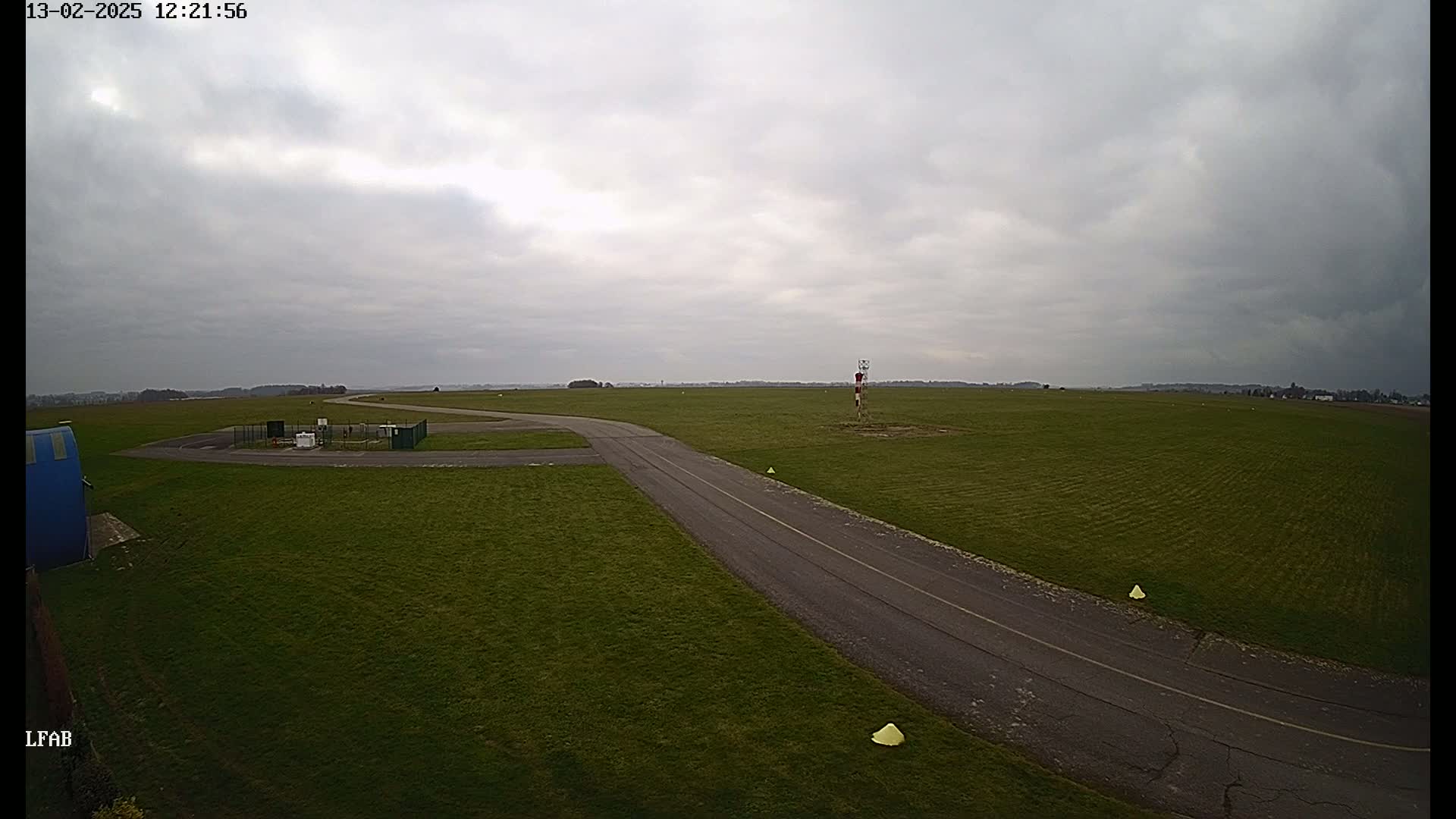A paved road curves through a grassy airfield under an overcast sky.