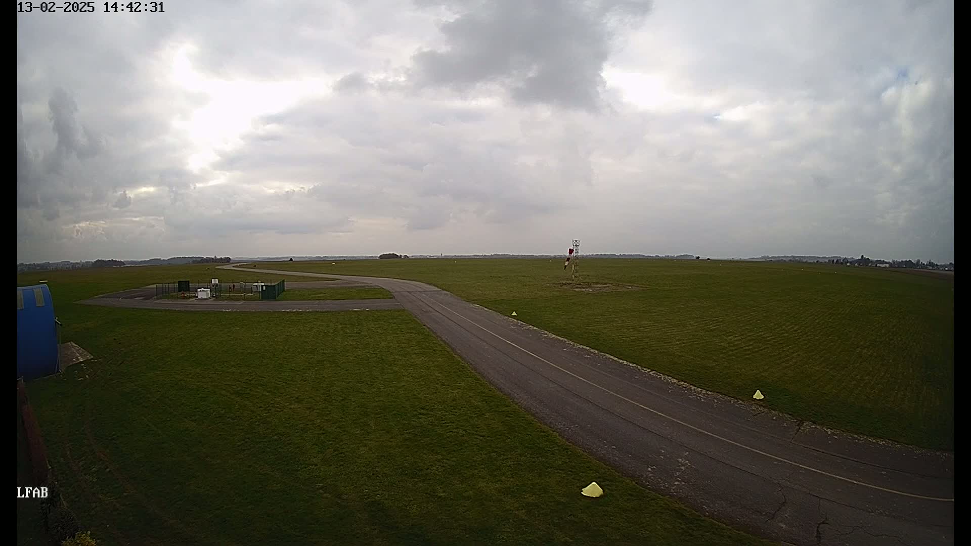 A paved taxiway curves through a grassy airfield under a mostly cloudy sky.