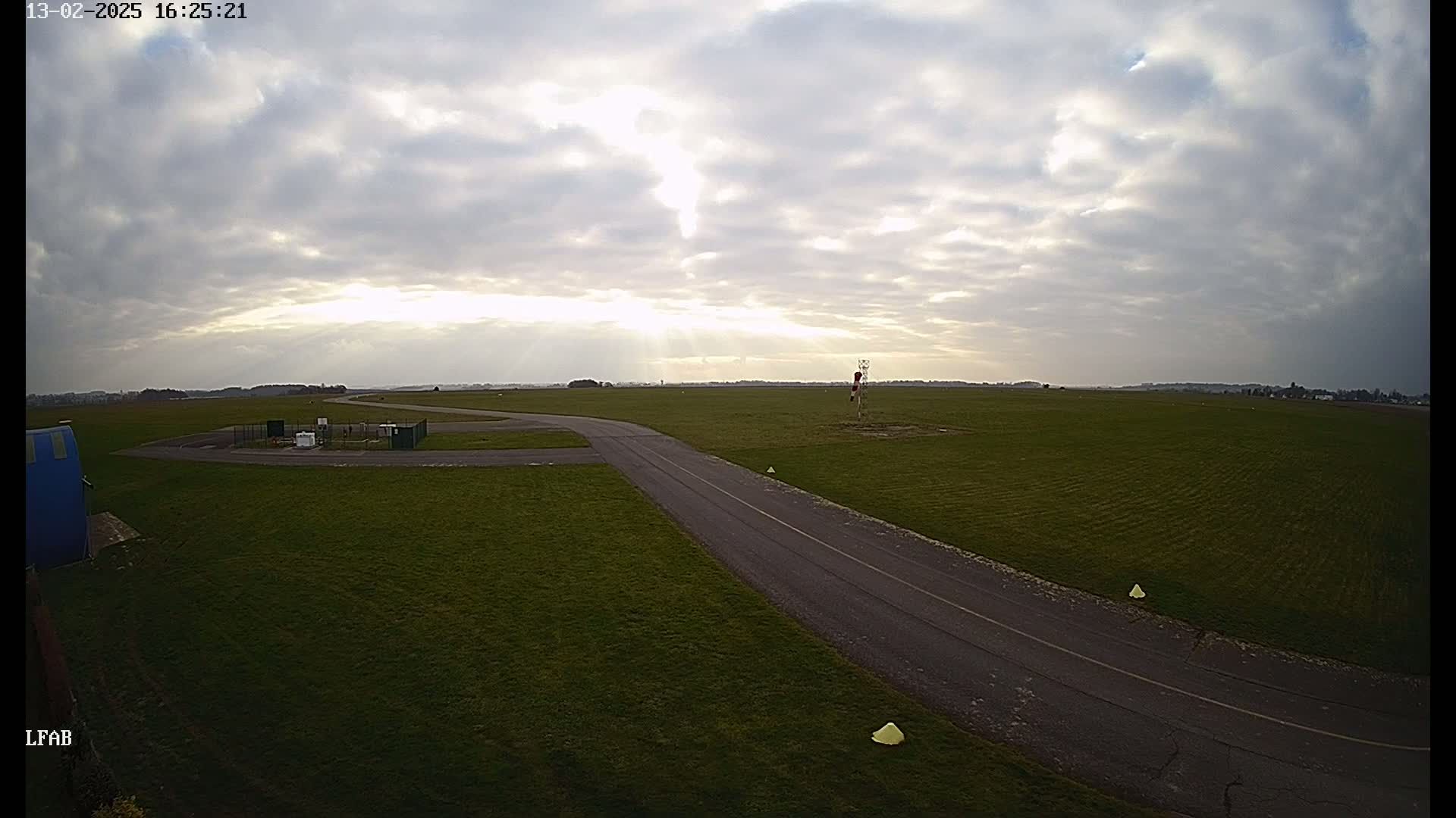 A paved road curves through a grassy airfield under a partly cloudy sky.