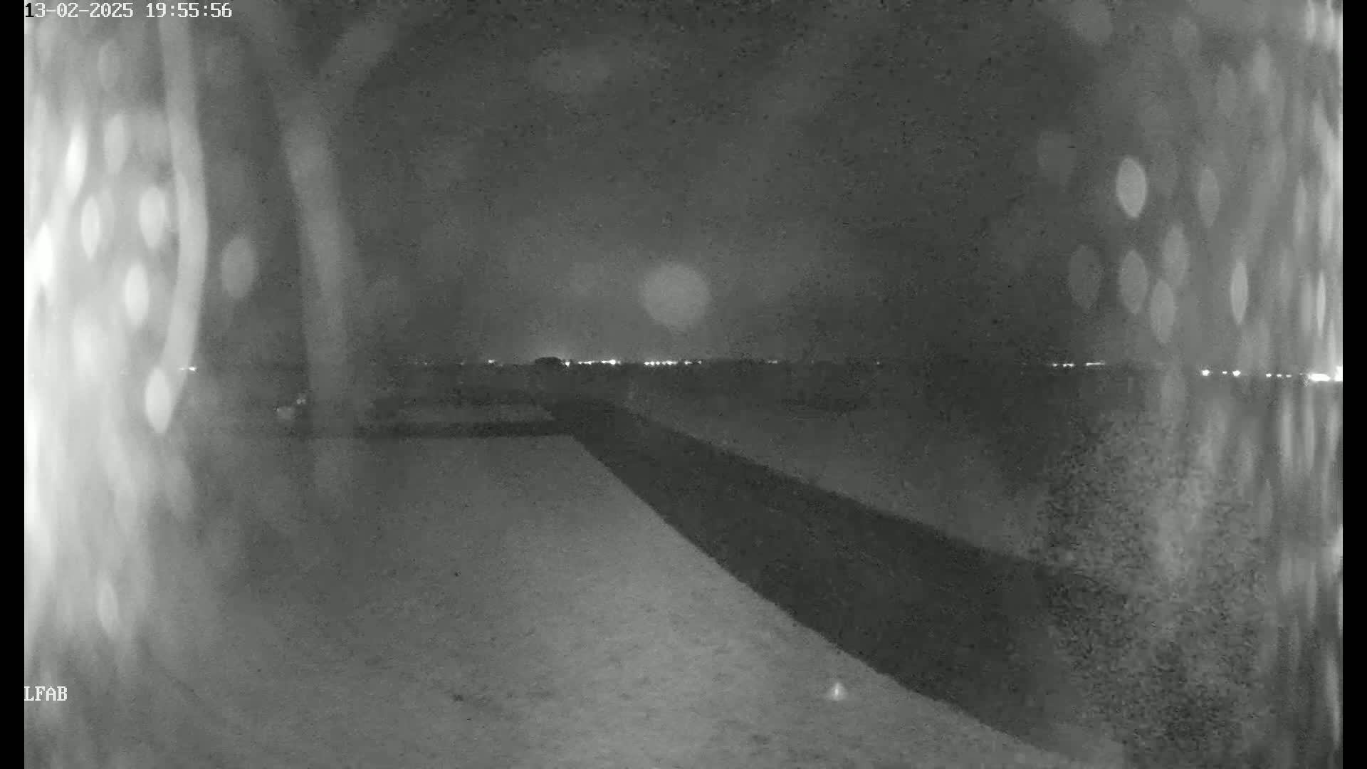 A nighttime, snow-covered ground stretches out toward a dimly lit horizon under a cloudy sky.
