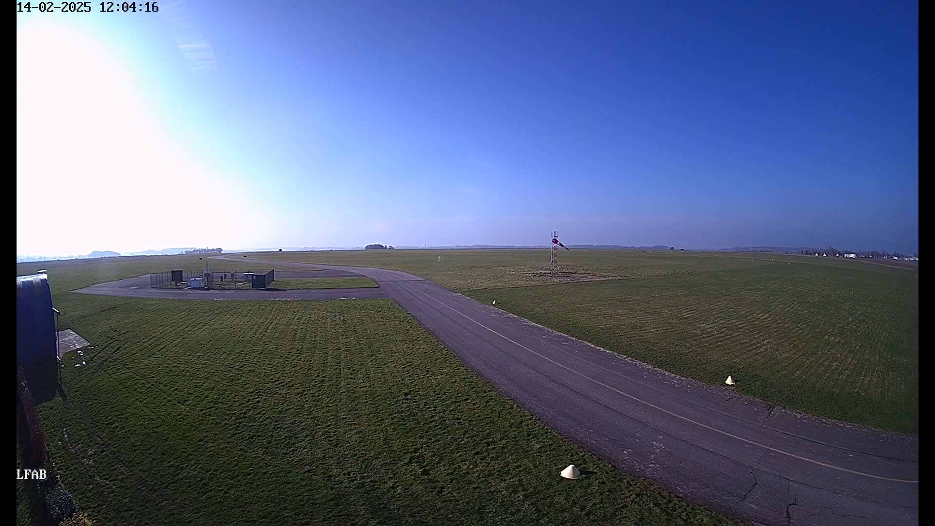A paved road curves through a grassy airfield under a clear blue sky.