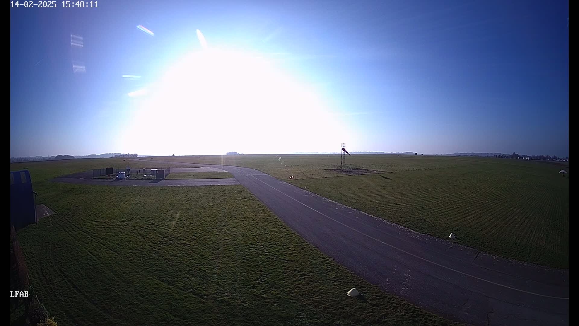 A paved road curves through a grassy airfield under a bright, sunny sky.