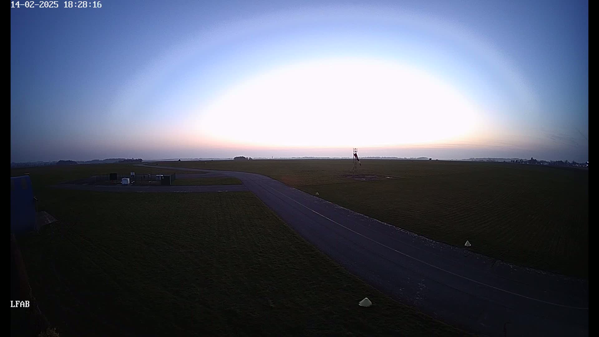 A paved taxiway curves through a grassy airfield at sunset under a clear, twilight sky.