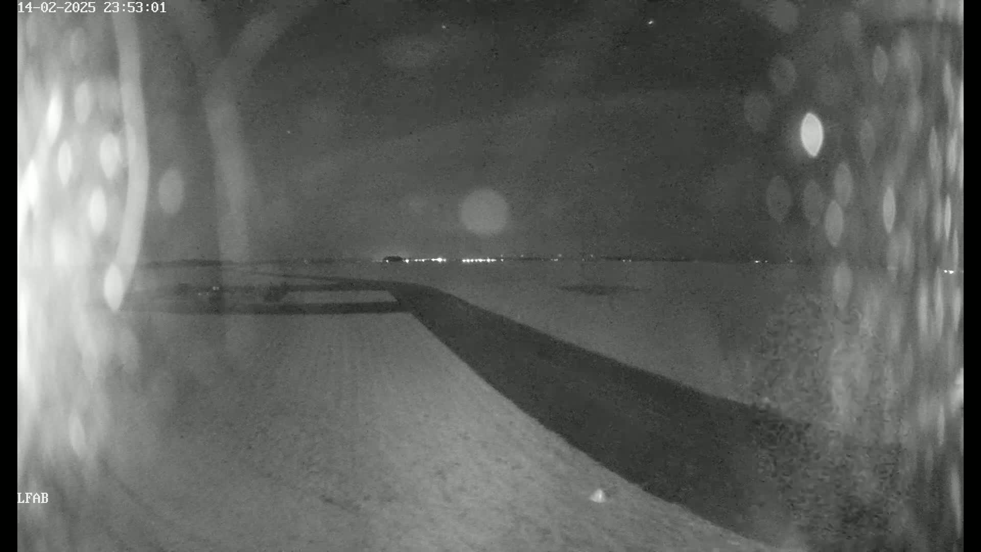 A nighttime, snow-covered landscape is visible, featuring a dark road curving into the distance towards a faint line of lights on the horizon under a dark sky.