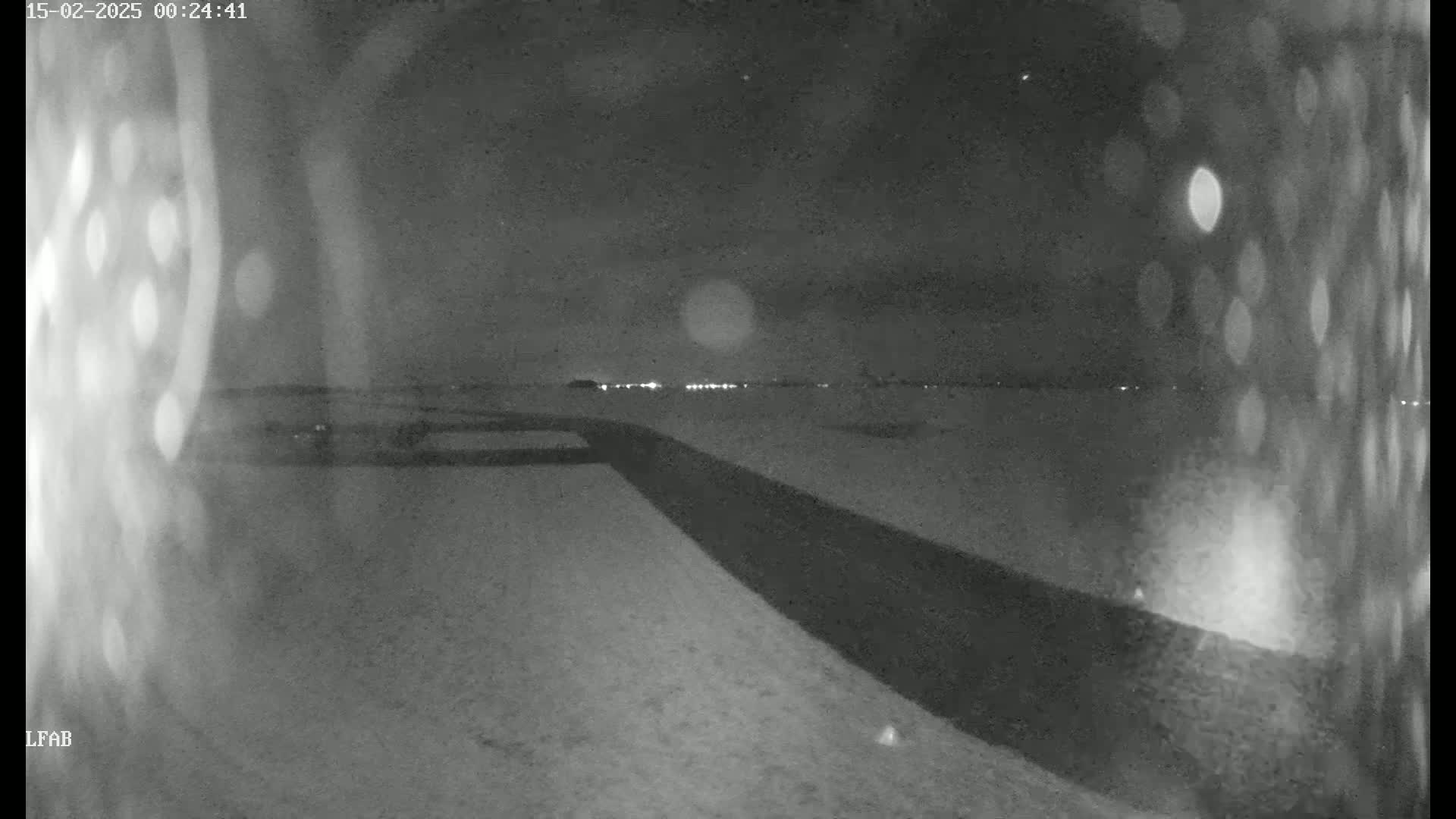 A nighttime, snow-covered landscape is visible, with a dark road or path extending from the foreground toward a distant line of lights under a cloudy sky.