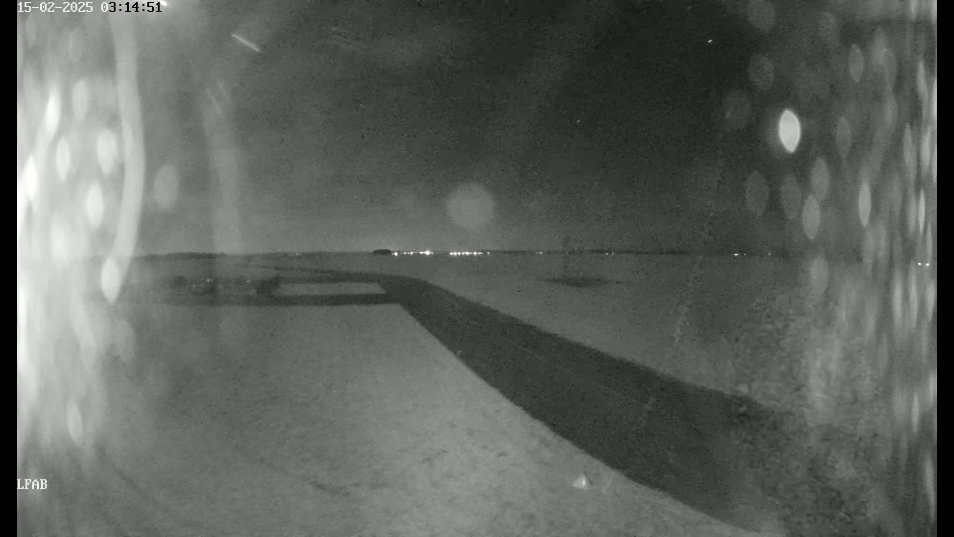 A snow-covered landscape is visible at night, with a dark road or path extending toward a distant line of lights.