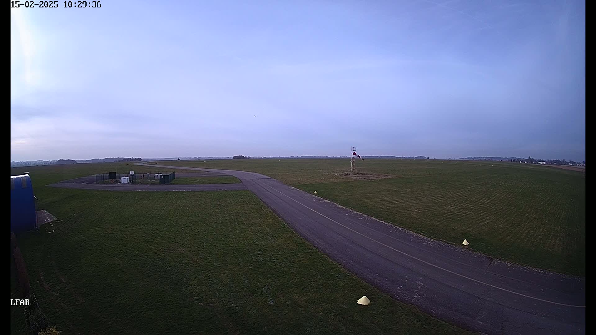 A paved taxiway curves across a grassy airfield under a clear, pale-blue sky.