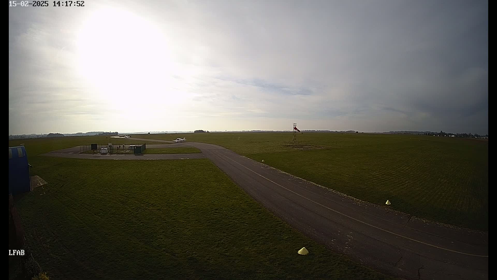 A small airplane sits on a grassy airfield under a mostly cloudy sky.