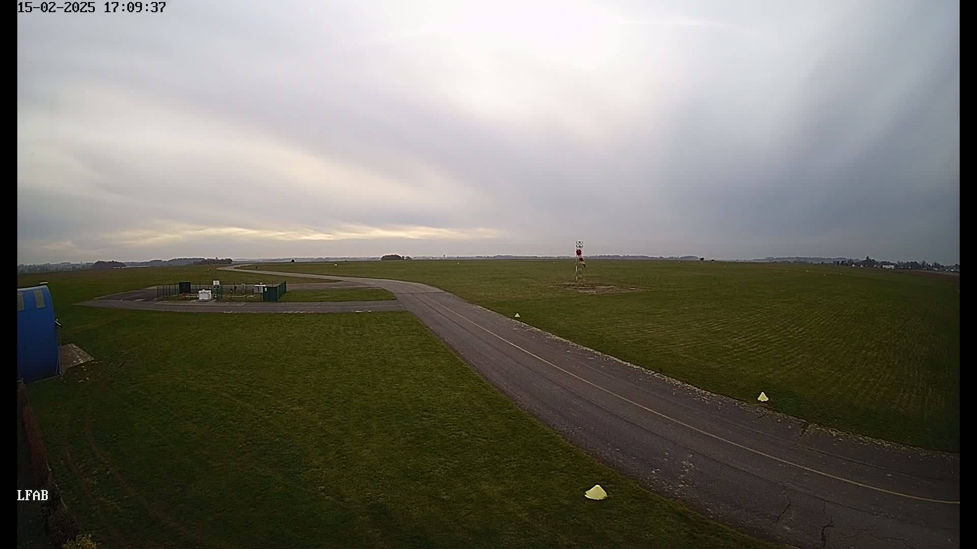 A paved road curves through a grassy airfield under an overcast sky.