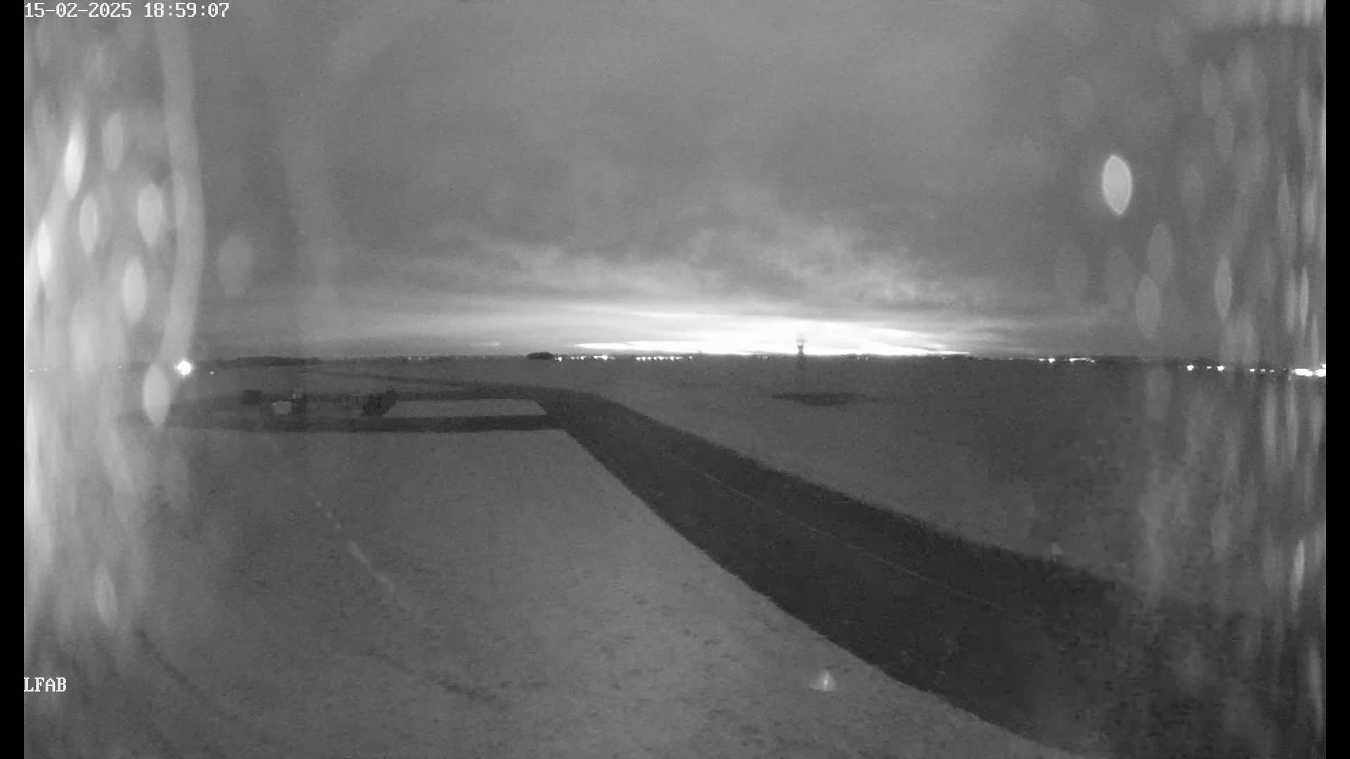 A snow-covered landscape at twilight shows a dark road extending into the distance, with faint lights visible on the horizon.