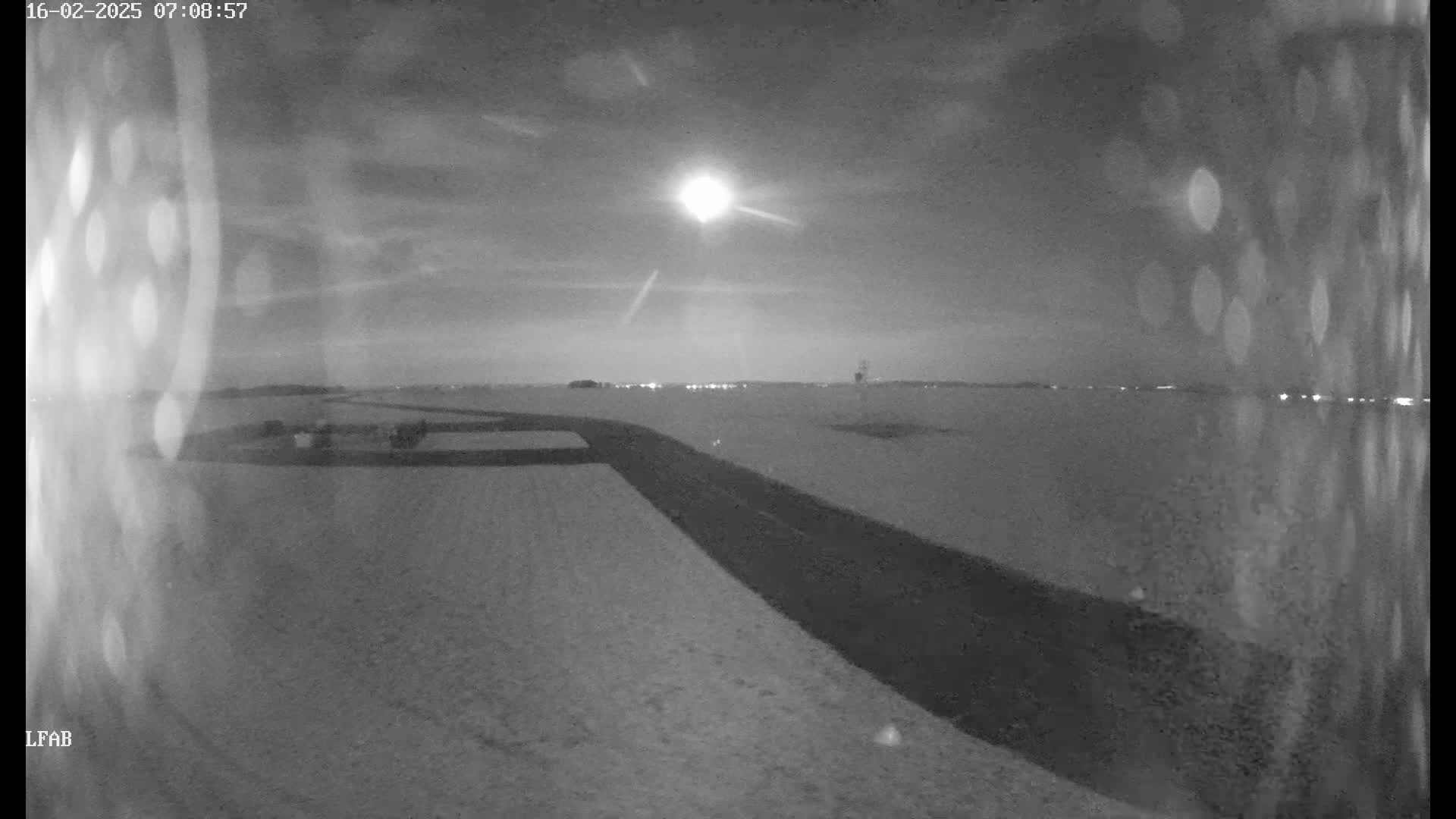 A snow-covered landscape at night is illuminated by a bright moon, showing a road curving through the scene.