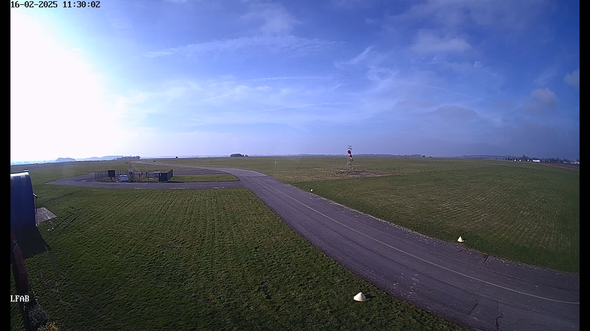 A paved road curves through a grassy airfield under a mostly clear, bright sky.
