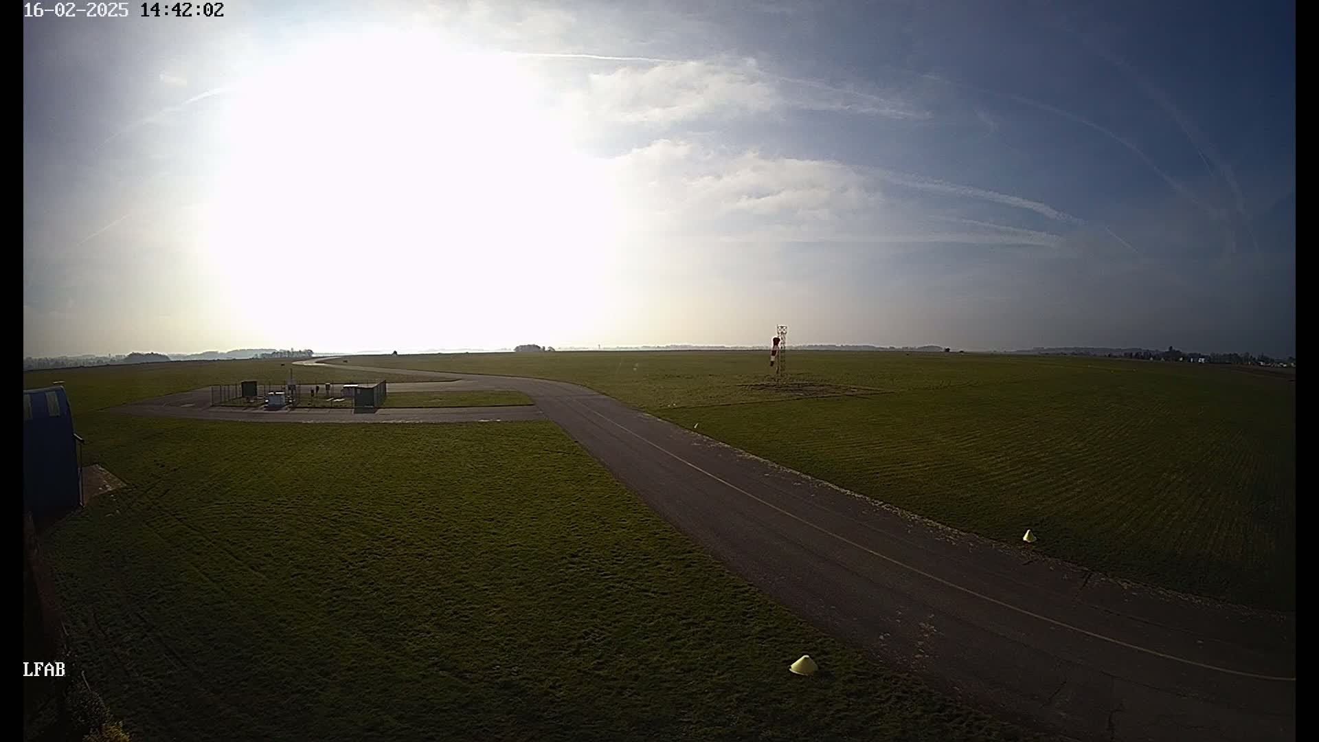 A paved road curves through a grassy airfield under a mostly sunny sky with a few scattered clouds.