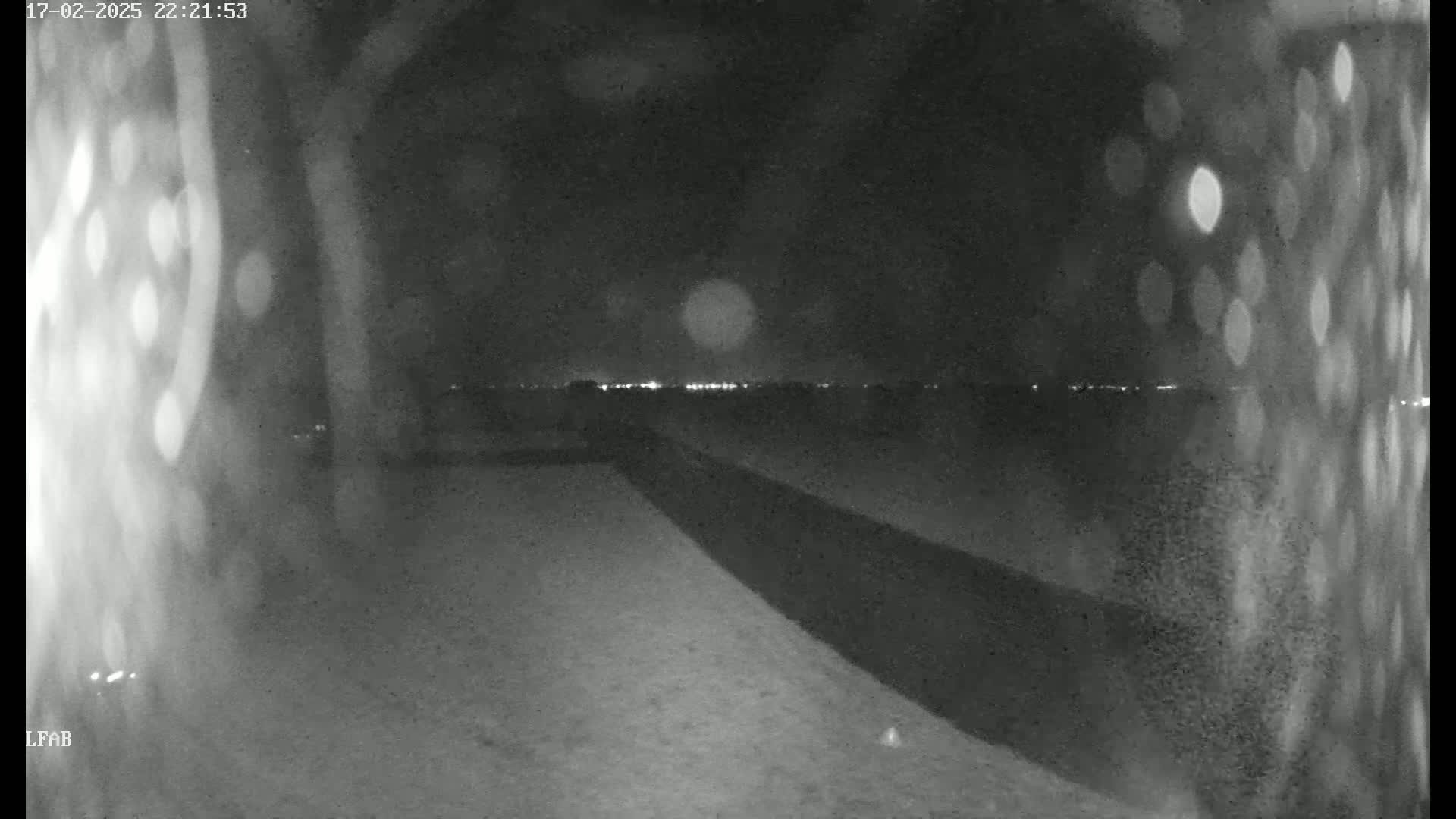 A nighttime, low-light view shows a snow-covered ground leading to a distant horizon illuminated by faint lights under a dark sky.