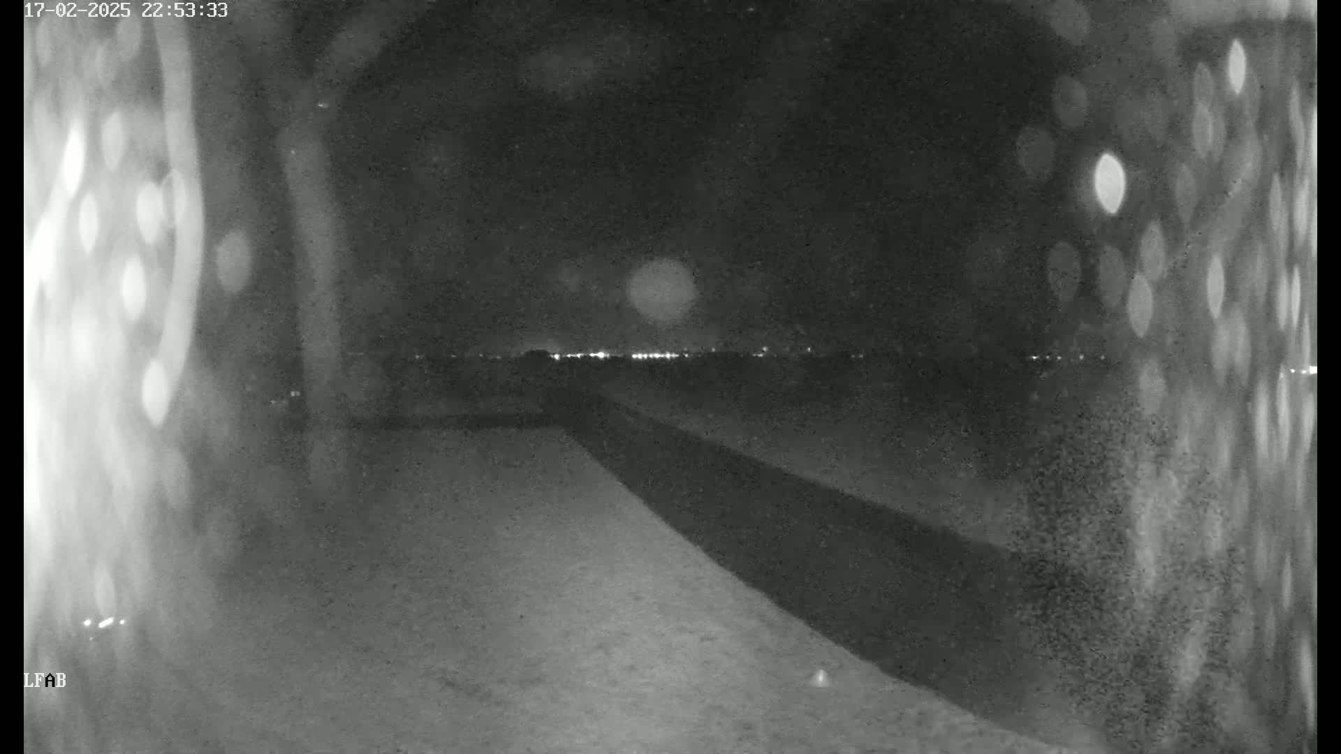A nighttime, low-light view of a dark road or path extending toward a distant horizon illuminated by faint lights.