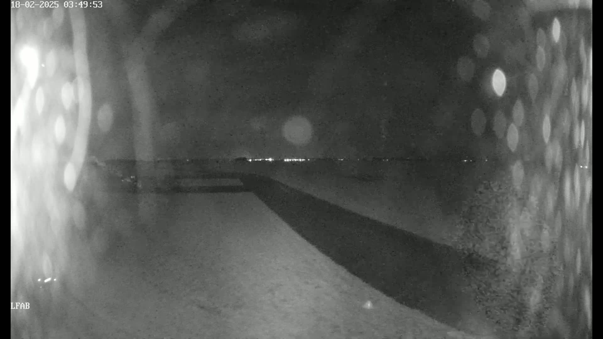 A nighttime, low-light view shows a flat, dark expanse of land extending toward a distant horizon with faint lights, possibly from a town or city.