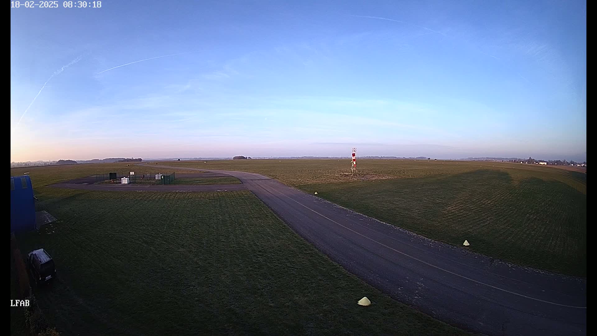 A paved road curves through a grassy airfield under a clear, light-blue sky.