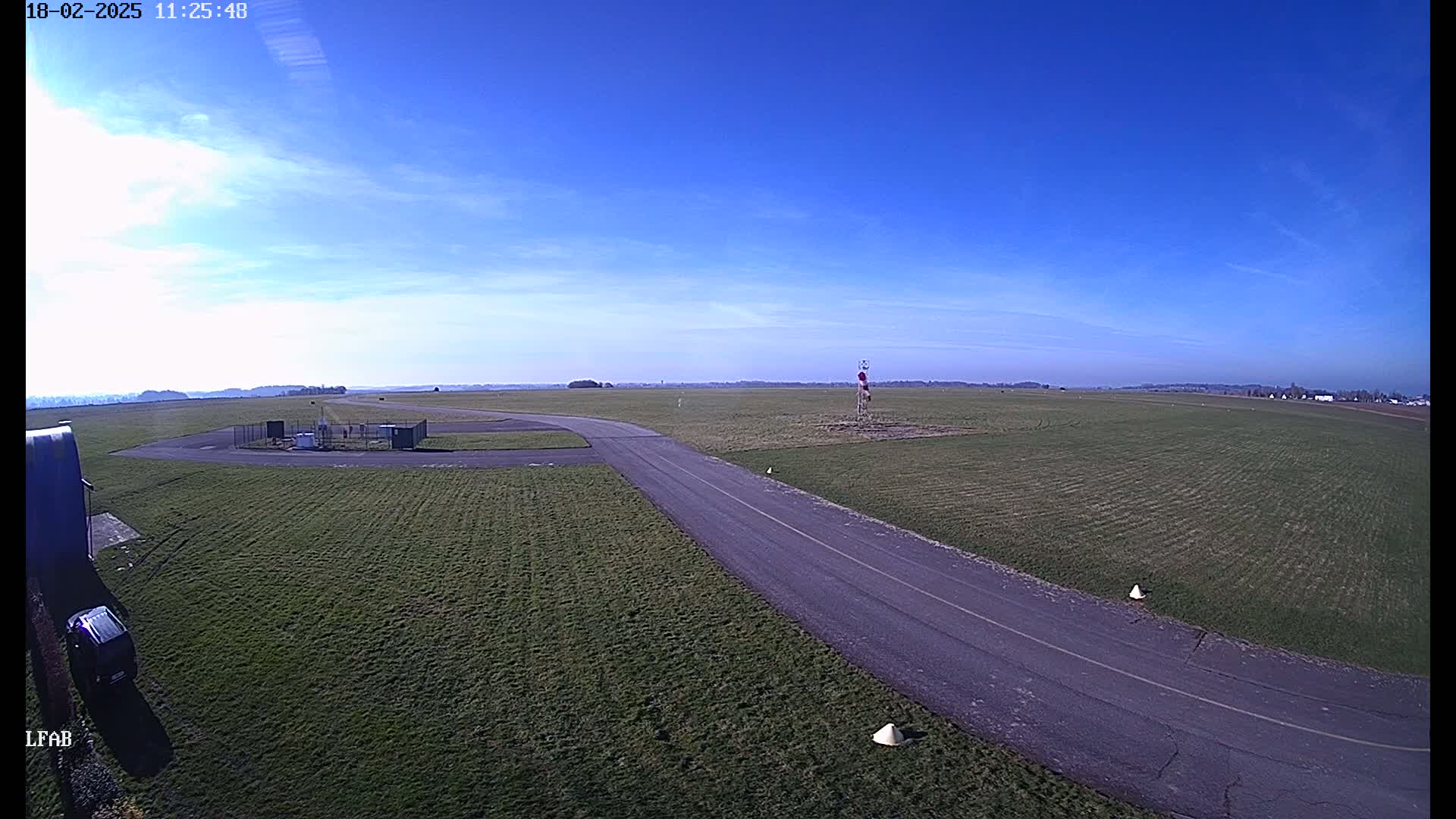 A paved taxiway curves across a grassy airfield under a mostly clear blue sky.