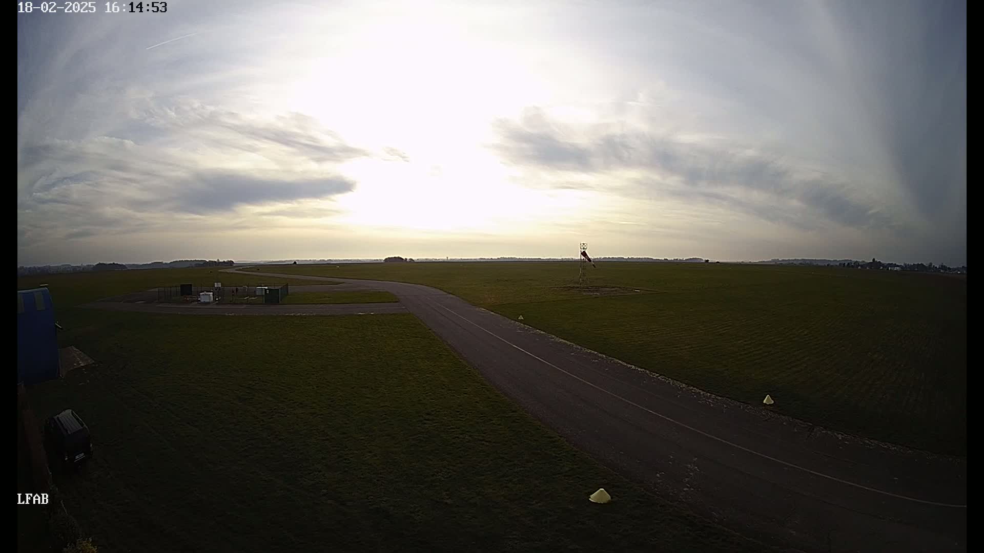 A paved taxiway curves across a grassy airfield under a partly cloudy sky.
