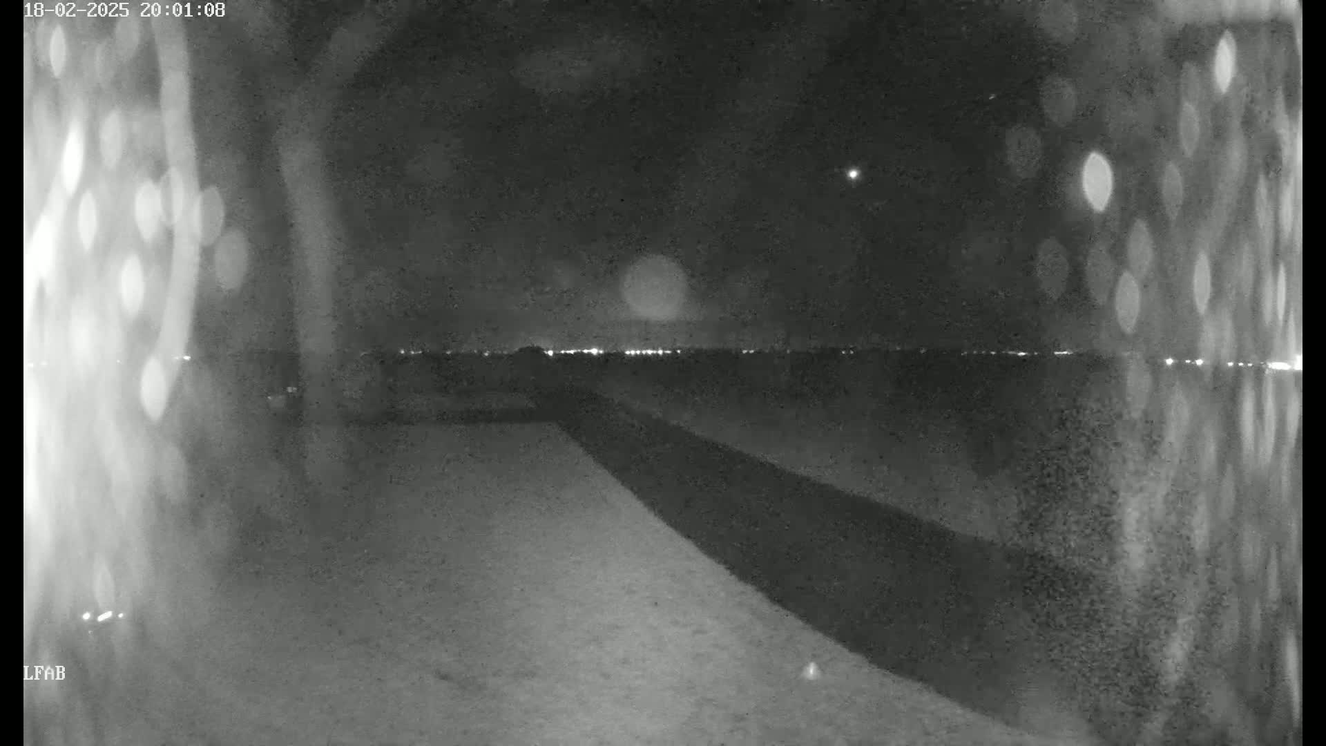 A nighttime, low-light view shows a dark road extending into the distance toward a faintly lit horizon under a mostly clear sky.