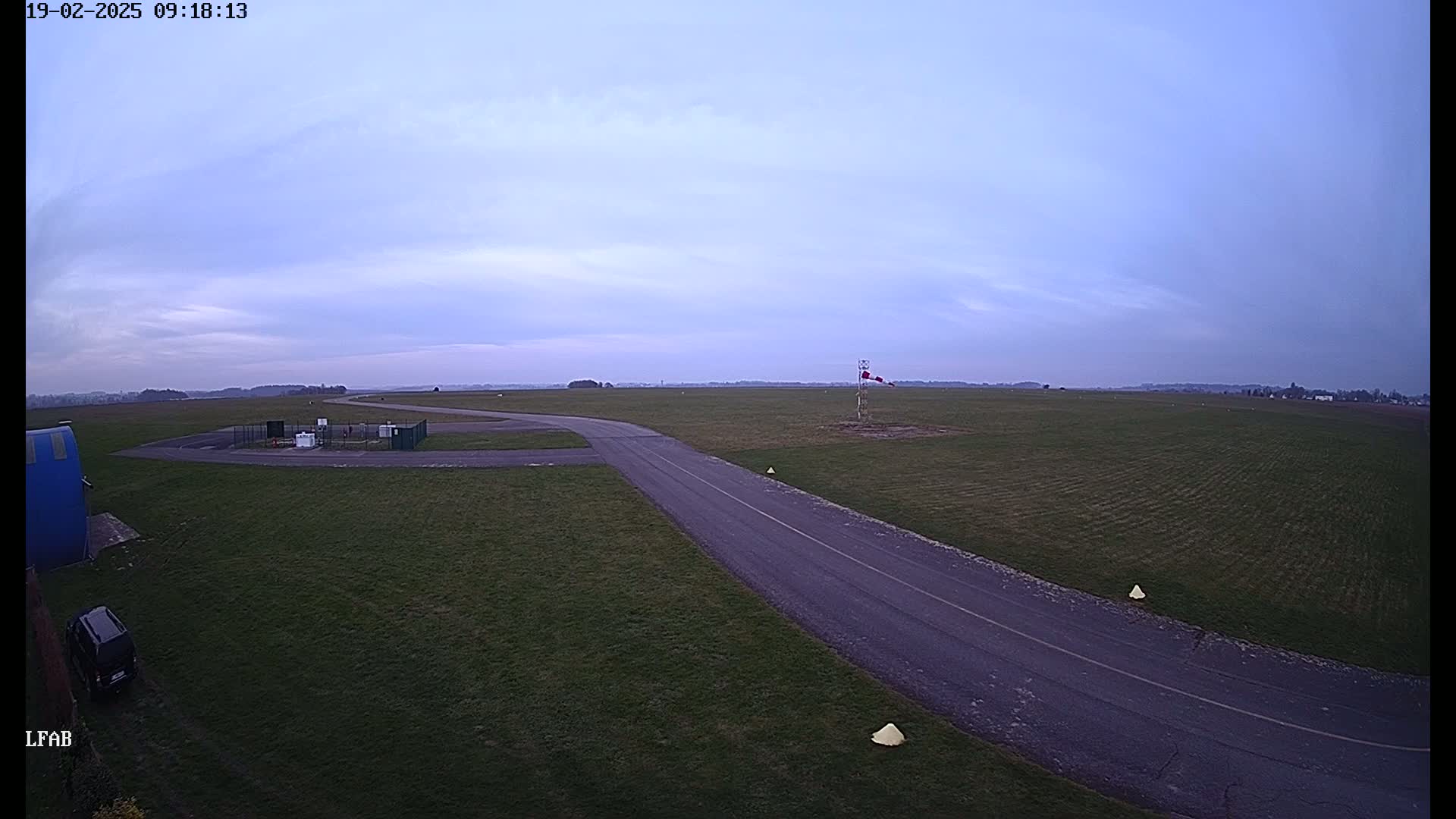 A paved road curves through a grassy airfield under a pale, overcast sky.