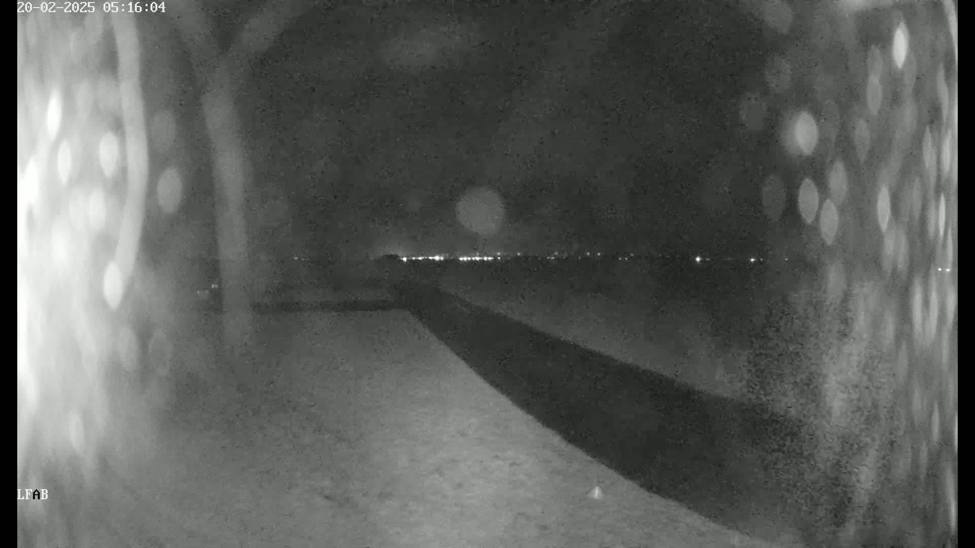 A nighttime, low-light image shows a dark, paved road or path extending into the distance toward a faintly lit horizon.