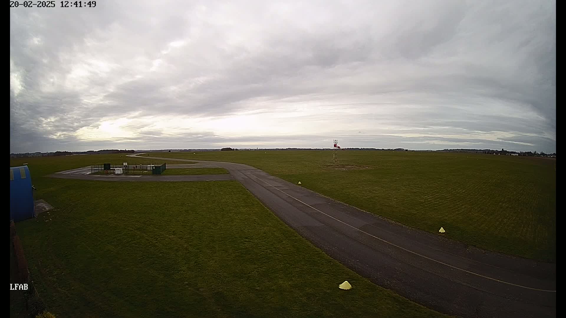 An airfield with a paved taxiway and grassy areas is visible under a mostly cloudy sky.