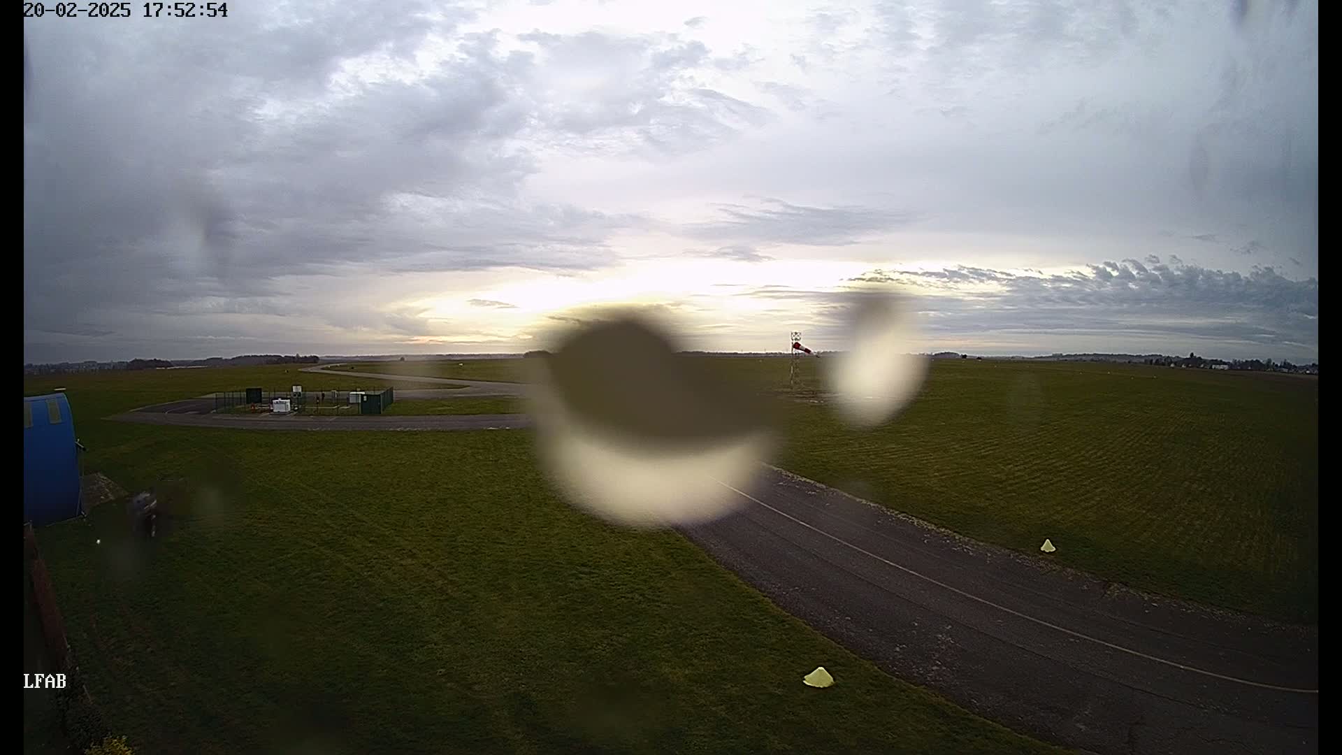 A view of a grassy airfield under a cloudy, overcast sky, with rain drops obscuring the view.
