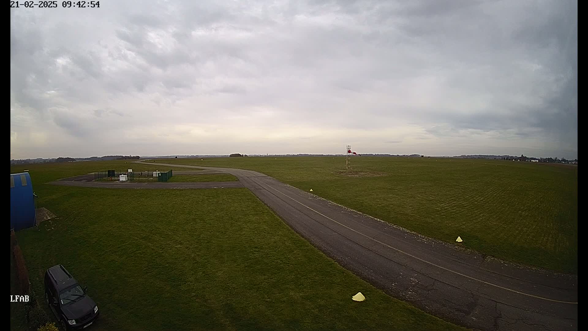 An airfield with a paved taxiway is shown on an overcast day.