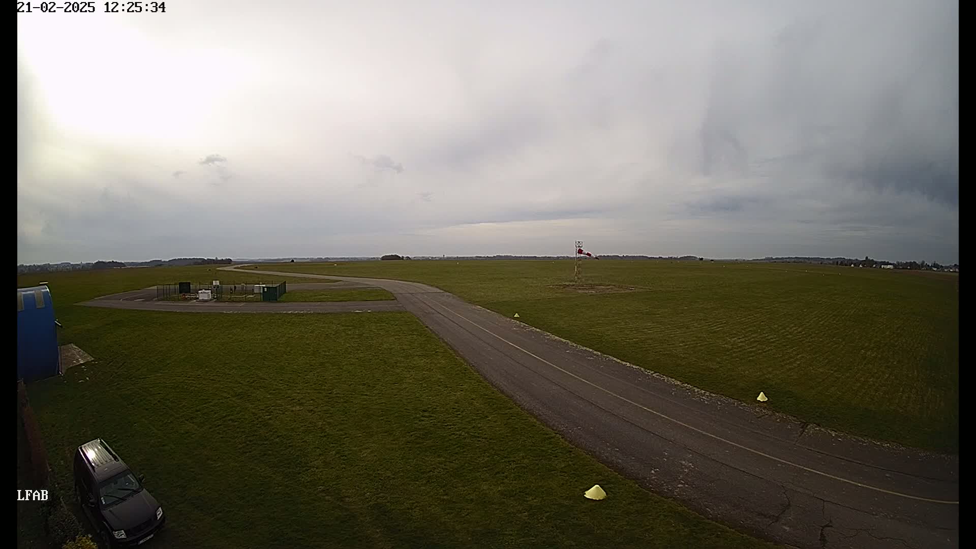 A paved taxiway curves through a grassy airfield under an overcast sky.