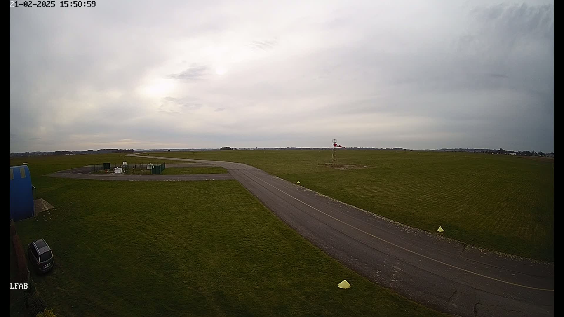 A paved taxiway curves across a grassy airfield under an overcast sky.