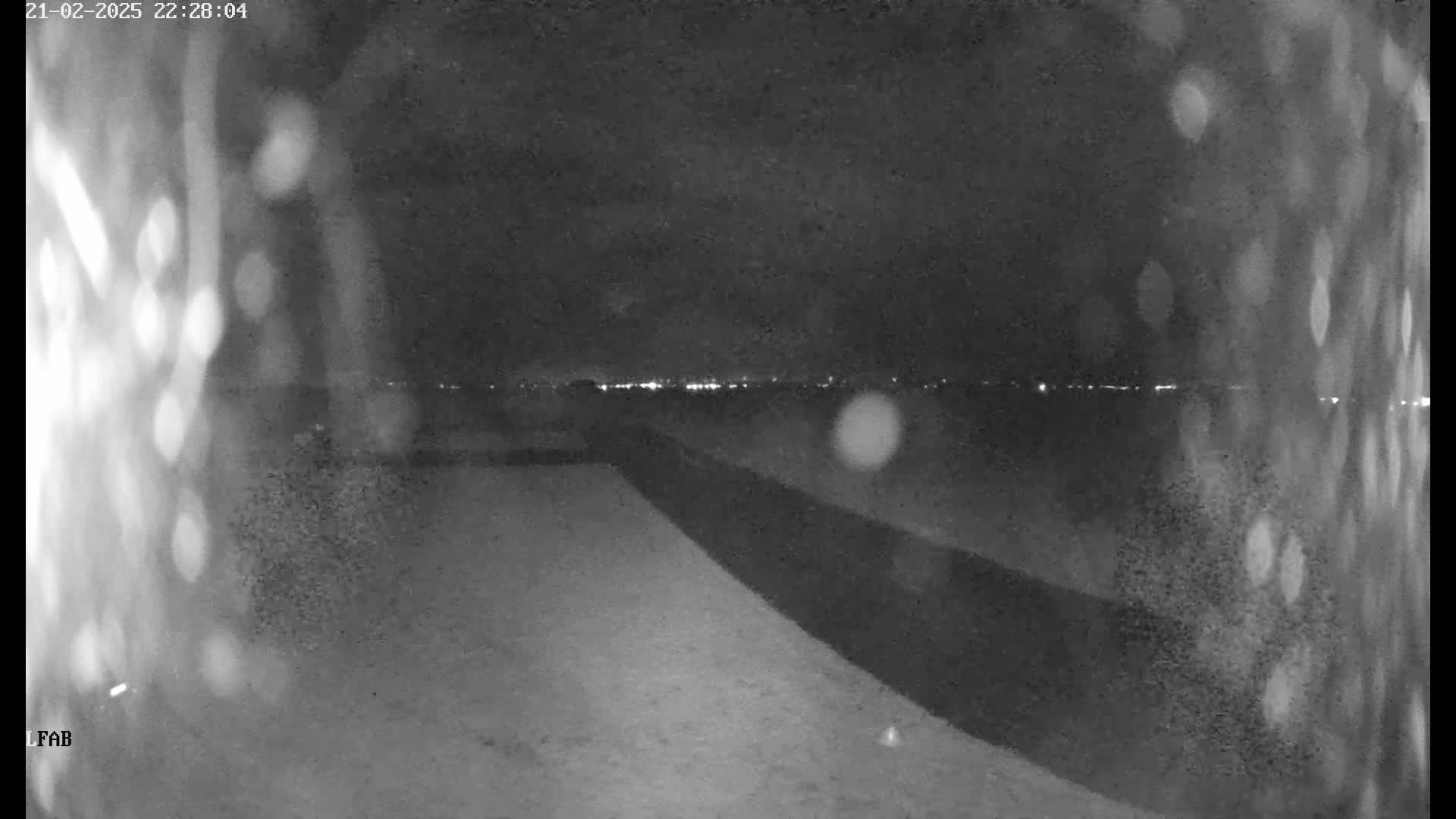 A nighttime, blurry view shows a dark, snow-covered ground sloping down towards a distant horizon where city lights are visible.