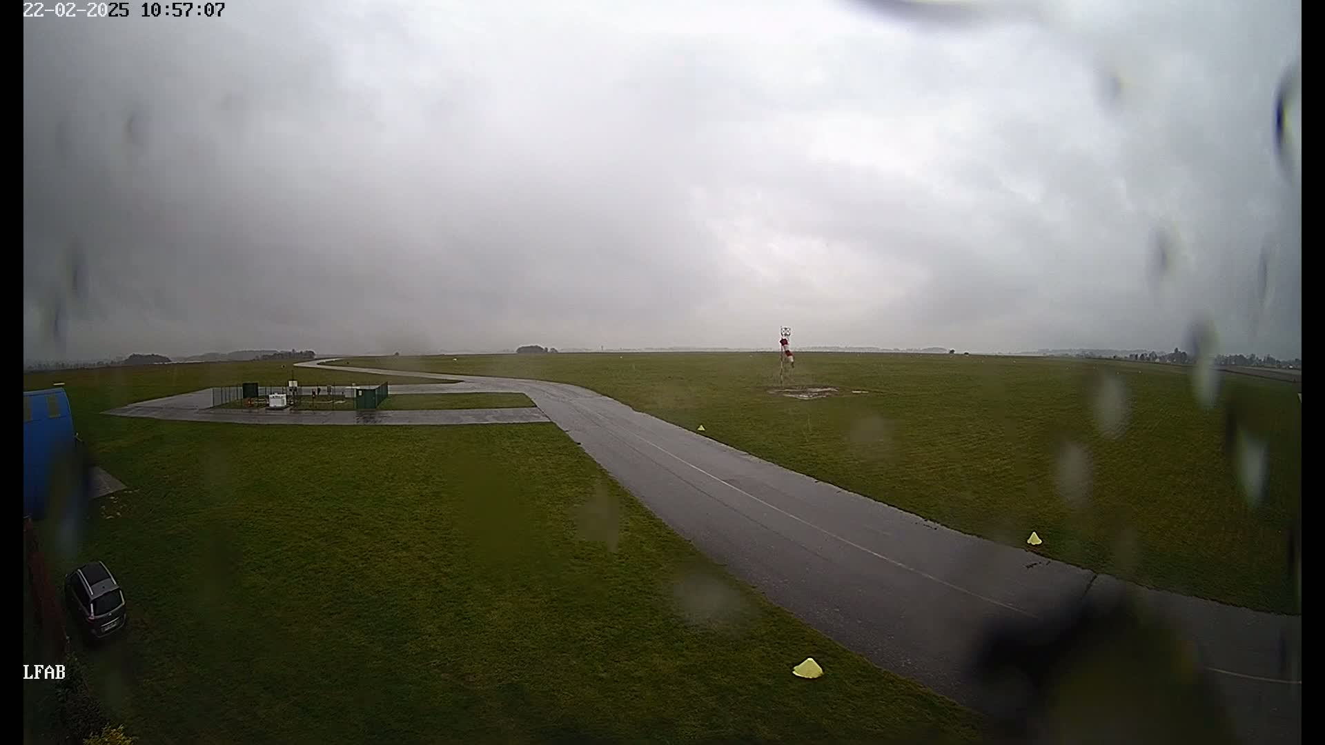 A rain-slicked tarmac taxiway curves through a grassy airfield under a gray, overcast sky.