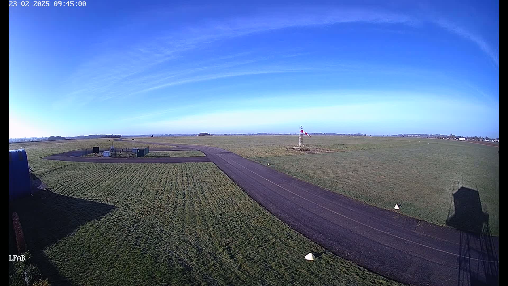 A paved runway curves through a grassy airfield under a clear blue sky.
