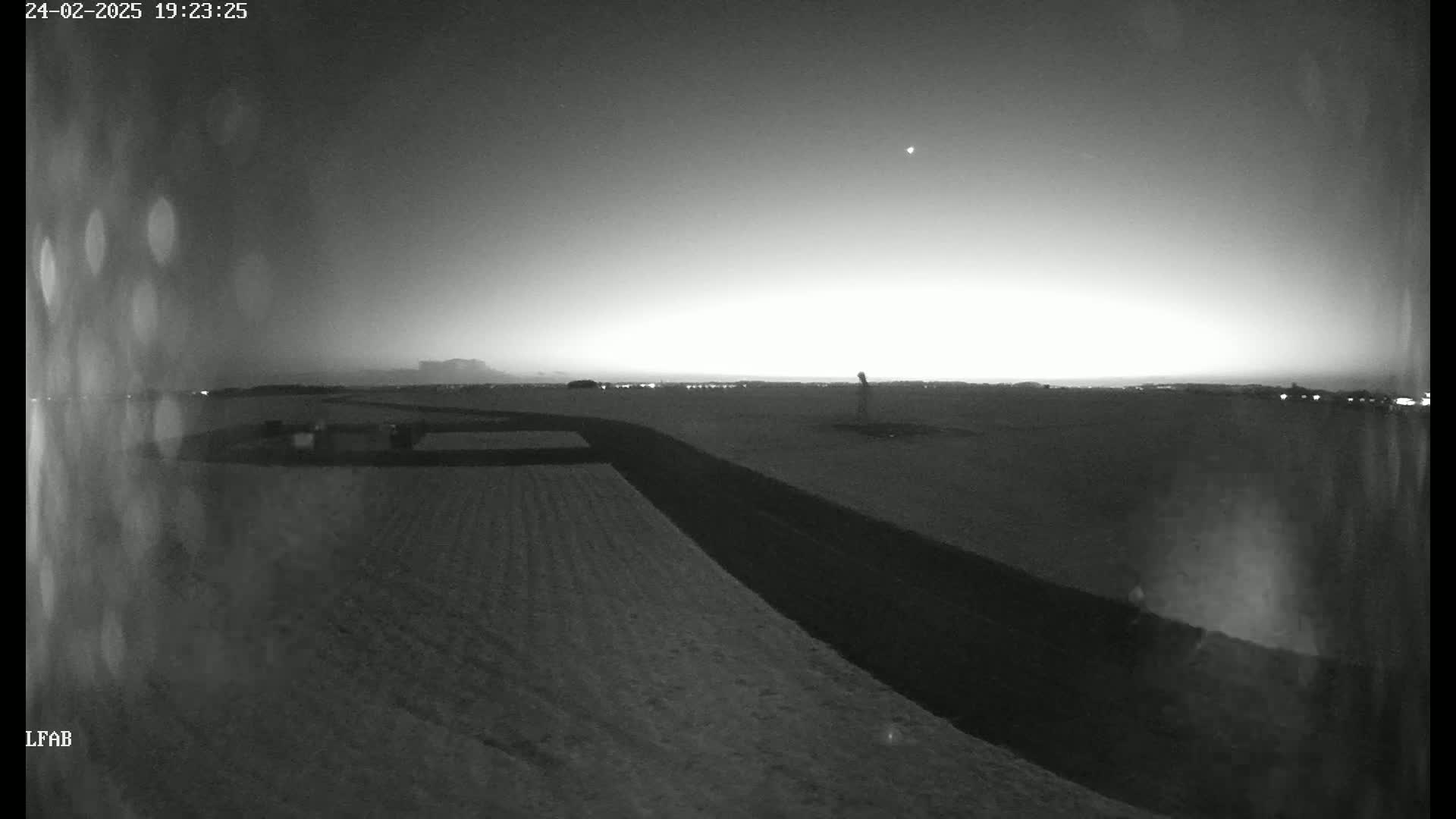 A nighttime, snow-covered field is dimly lit by a bright horizon, with a single light visible in the sky.