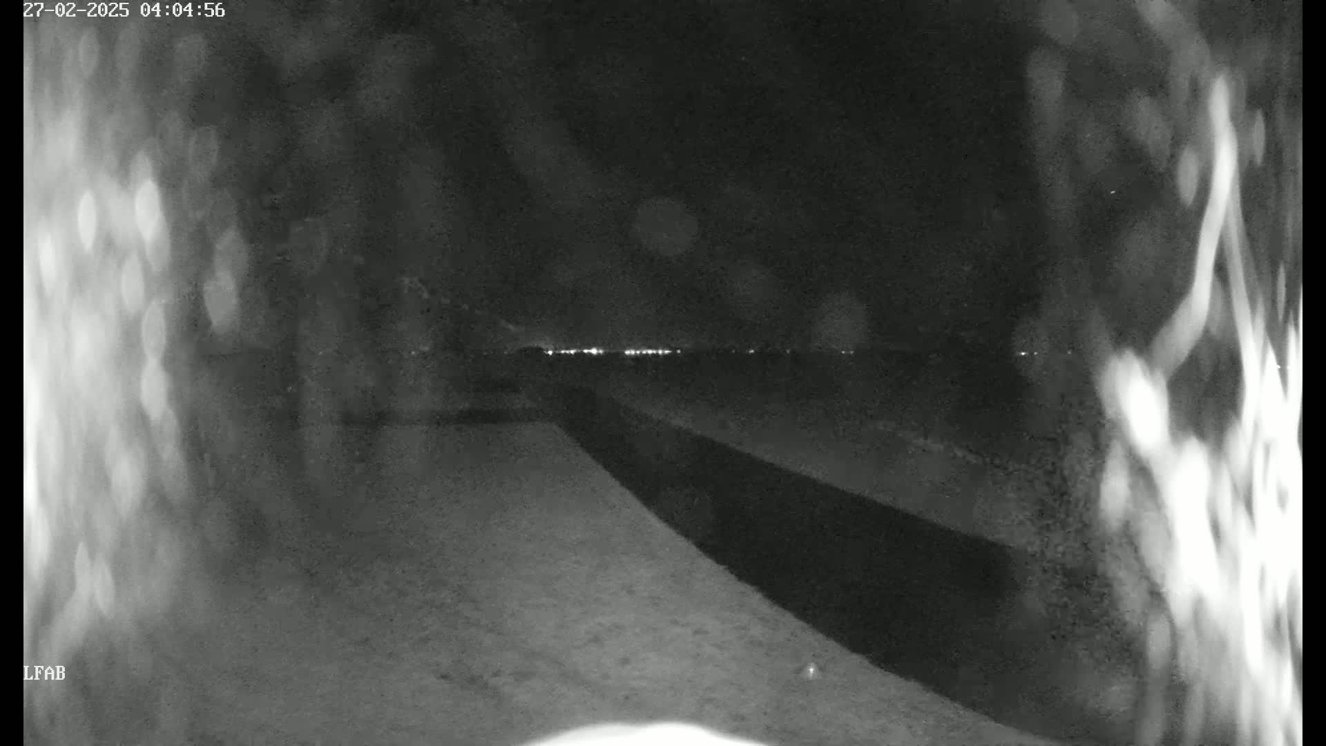 A nighttime, low-light view shows a dark, paved area extending toward a distant horizon where faint lights are visible.