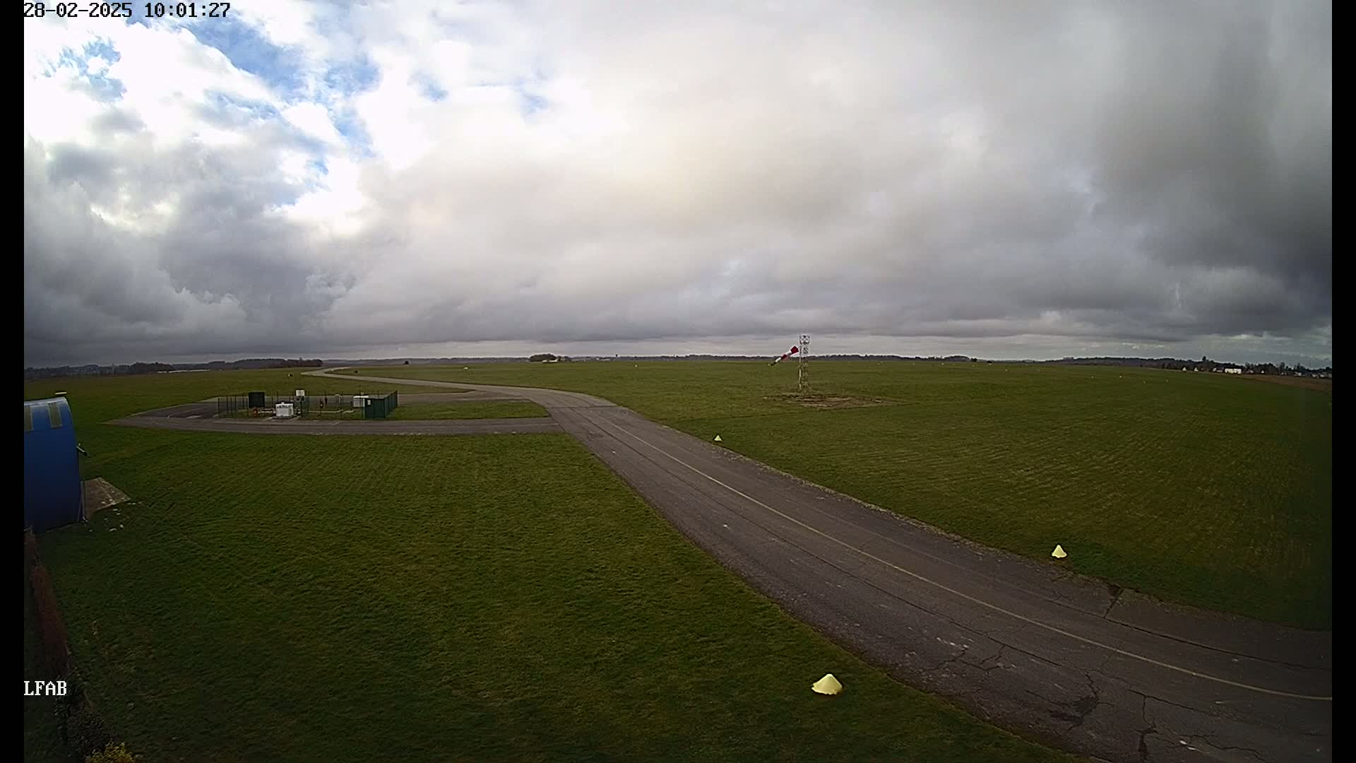 An airfield with a paved taxiway on a mostly cloudy day.