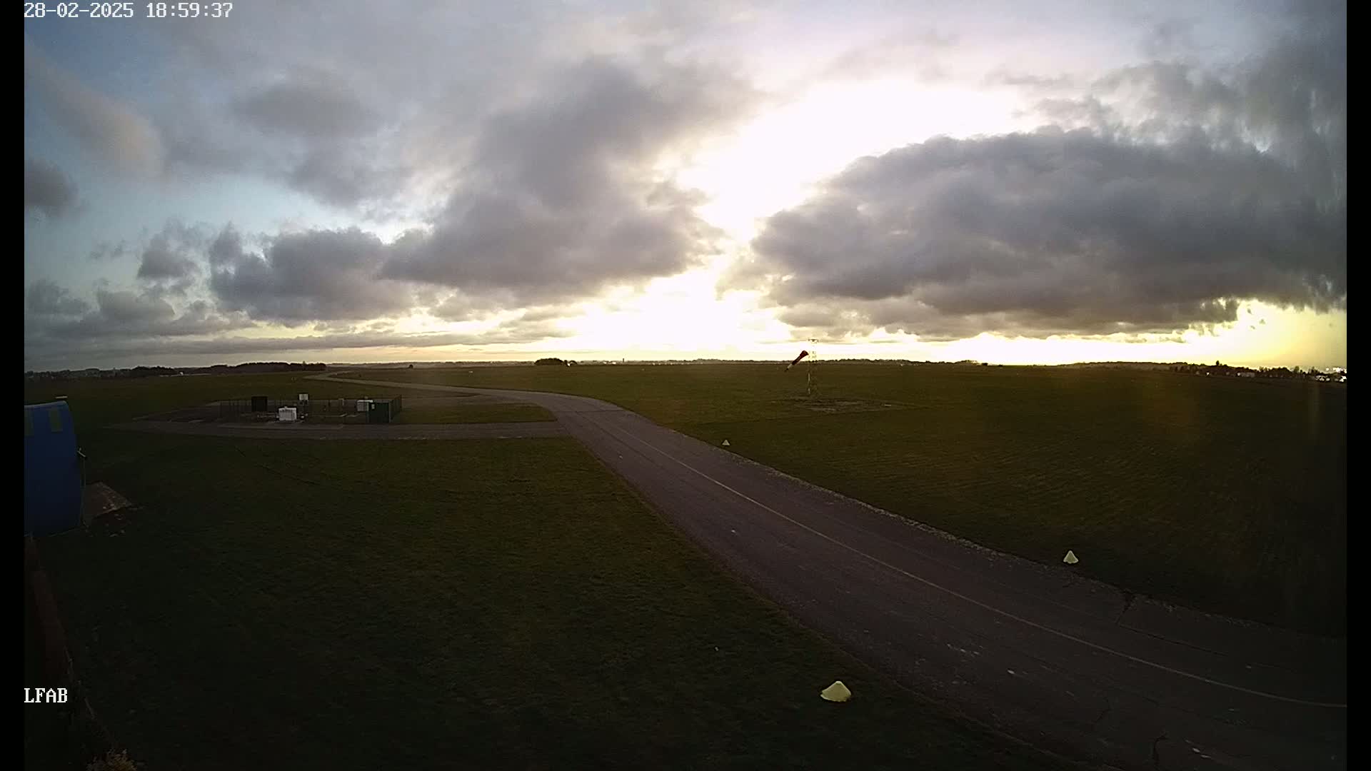 A paved taxiway curves through a grassy airfield under a partly cloudy sunset sky.