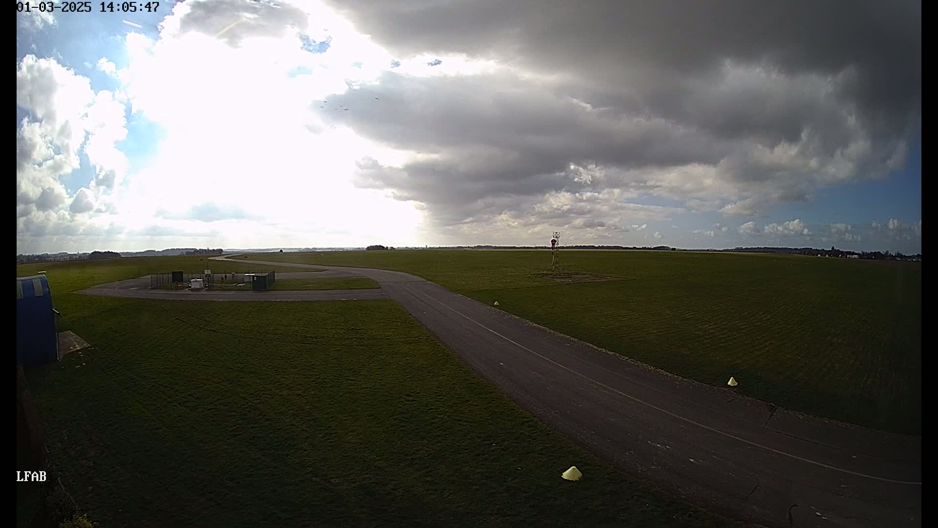 A paved taxiway curves through a grassy airfield under a partly cloudy sky.