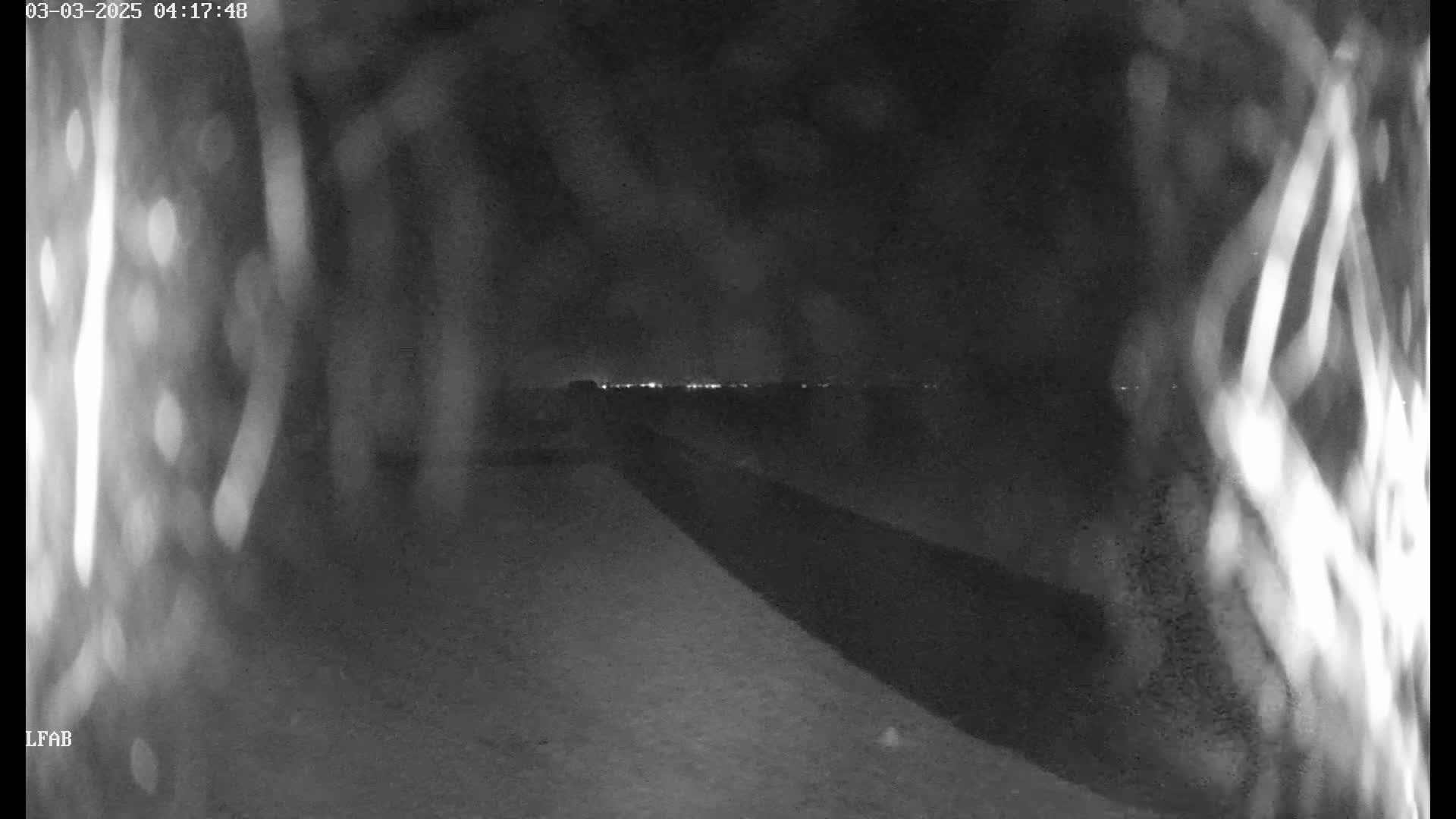 A nighttime view shows a dark, paved area leading toward a distant line of lights under a dark sky.