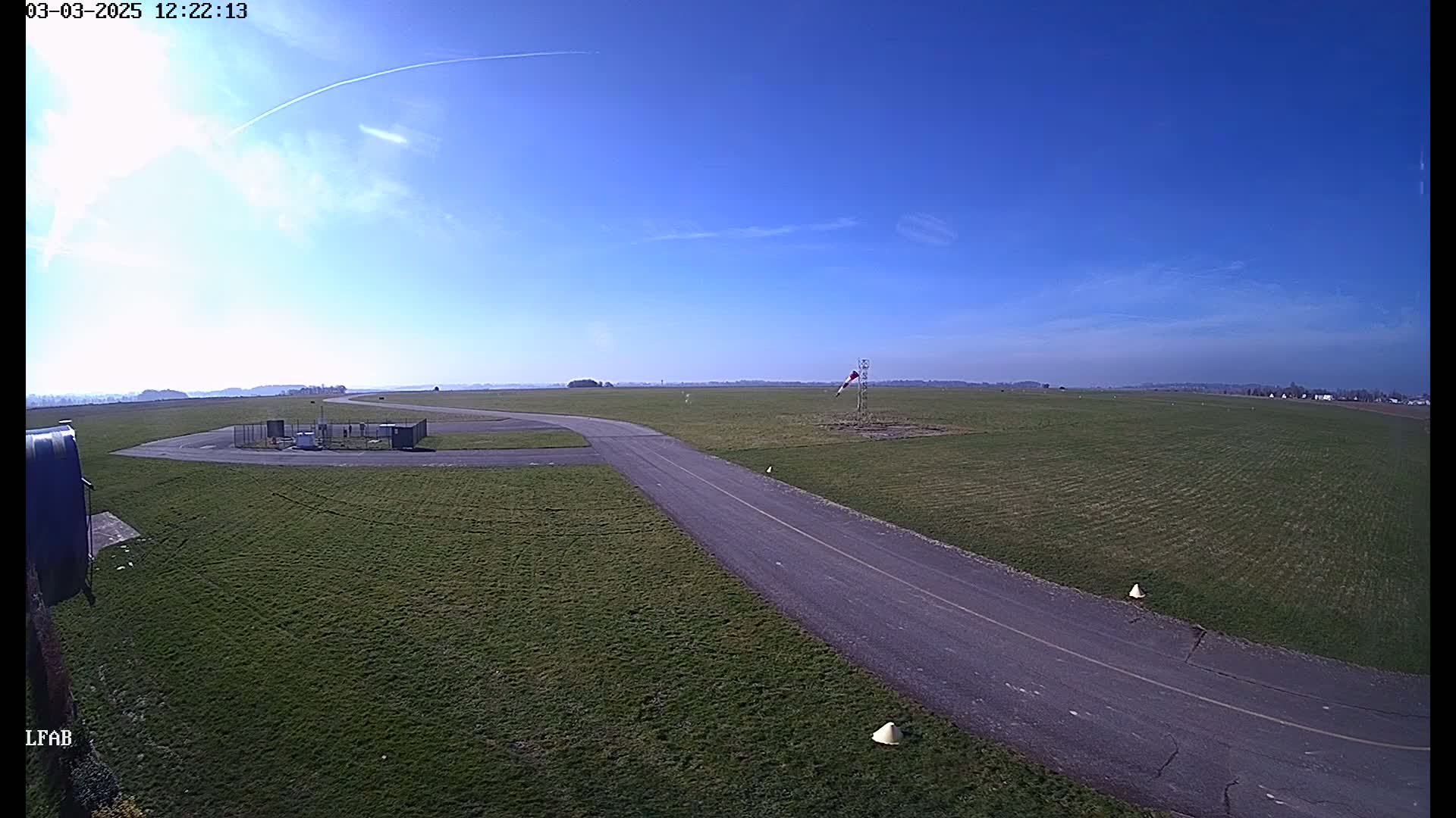 A paved taxiway curves across a grassy airfield under a mostly clear blue sky.