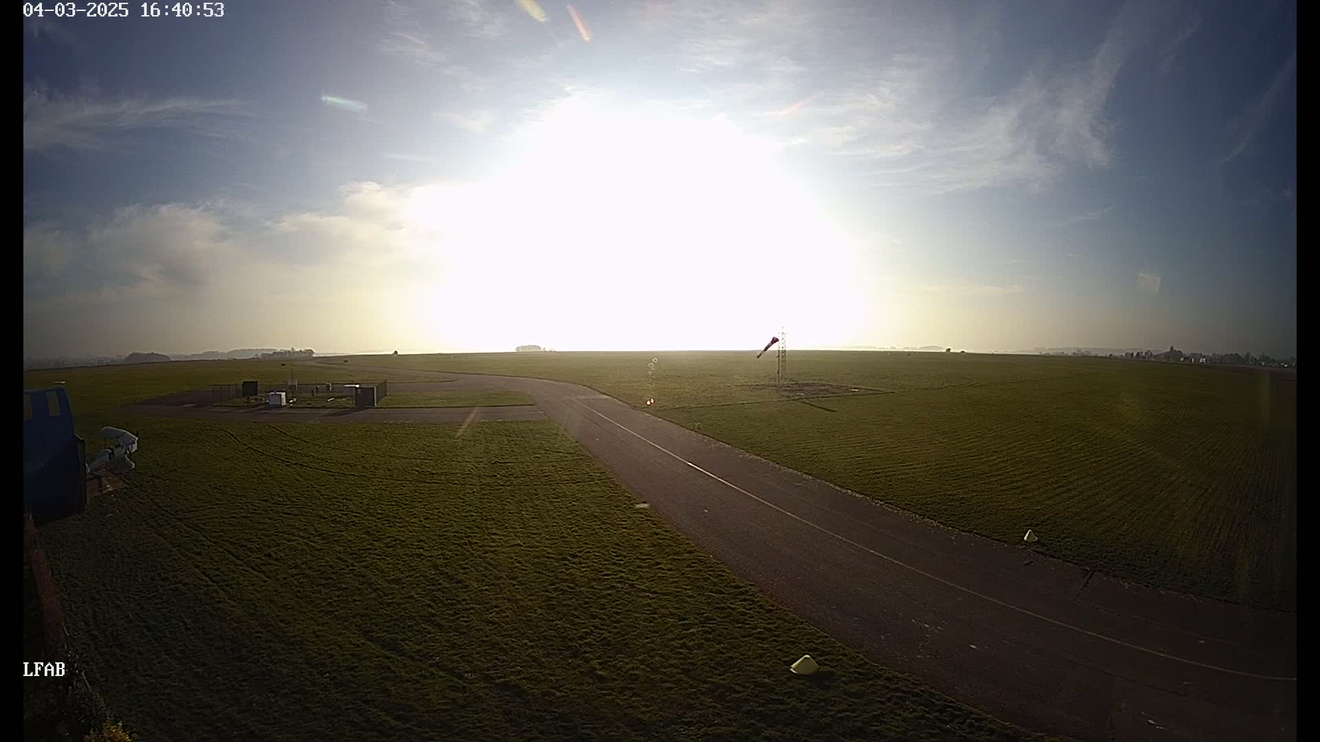 A paved road curves through a grassy airfield under a bright, mostly sunny sky.