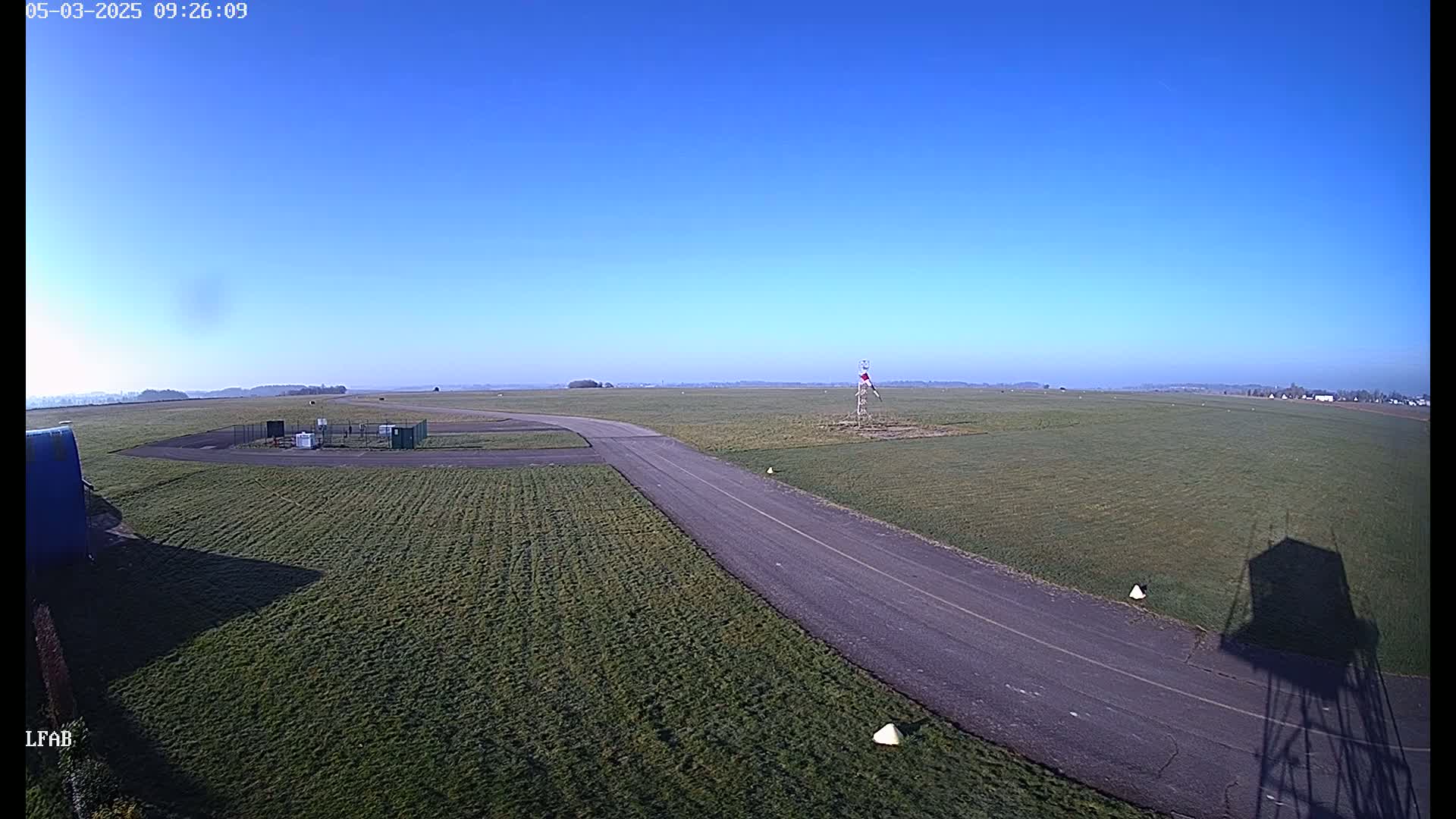 A paved road curves through a grassy airfield under a clear blue sky.