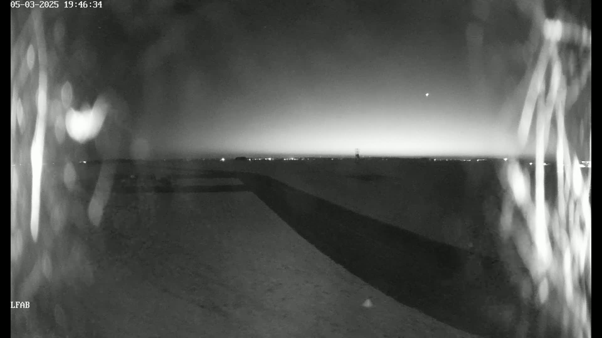 A dark, snowy landscape is visible at night, with a faint horizon showing distant lights under a mostly clear sky.