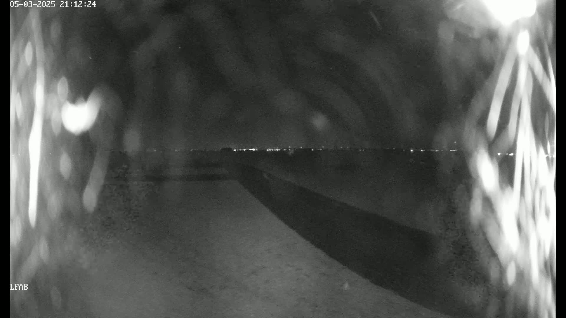 A nighttime, low-light view shows a dark road leading toward a distant horizon with faint city lights.