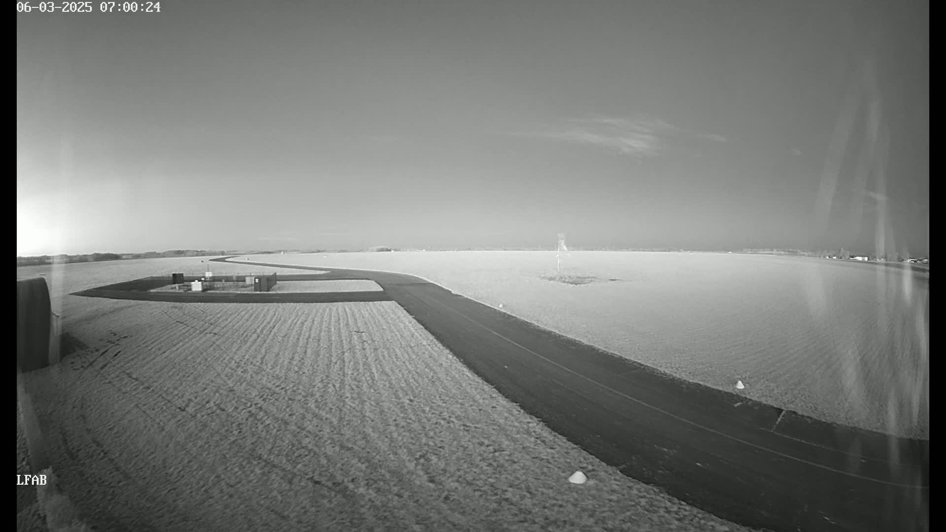A paved road curves through a flat, plowed field under a clear, light sky.