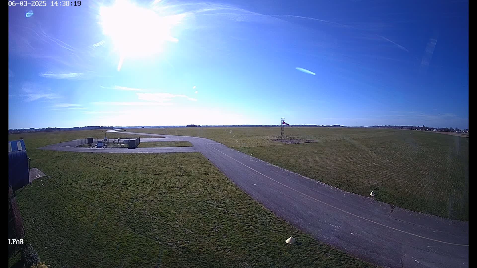 A paved roadway curves through a grassy airfield under a bright, sunny sky with few clouds.