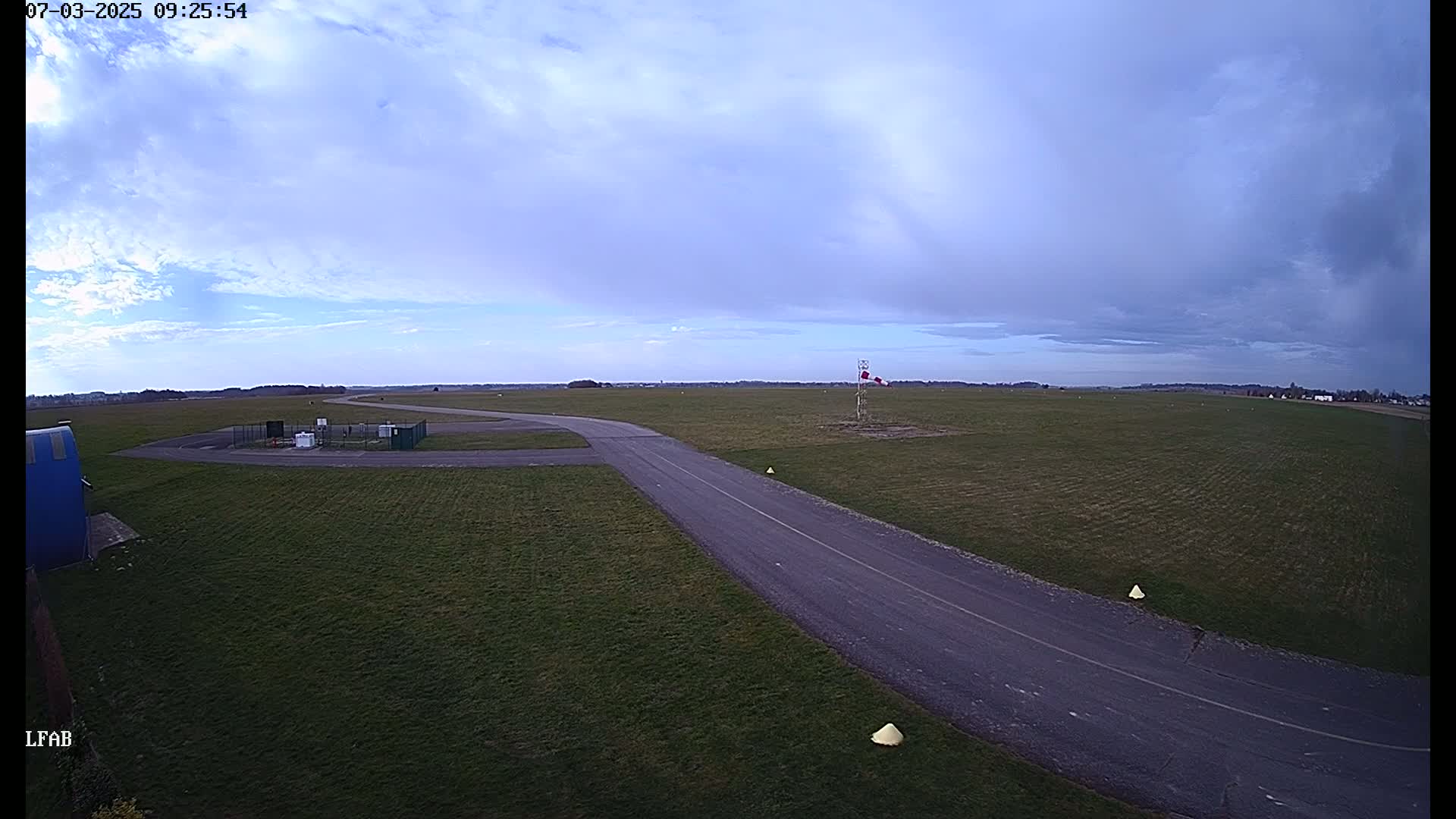 A paved taxiway winds through a grassy airfield under a partly cloudy sky.