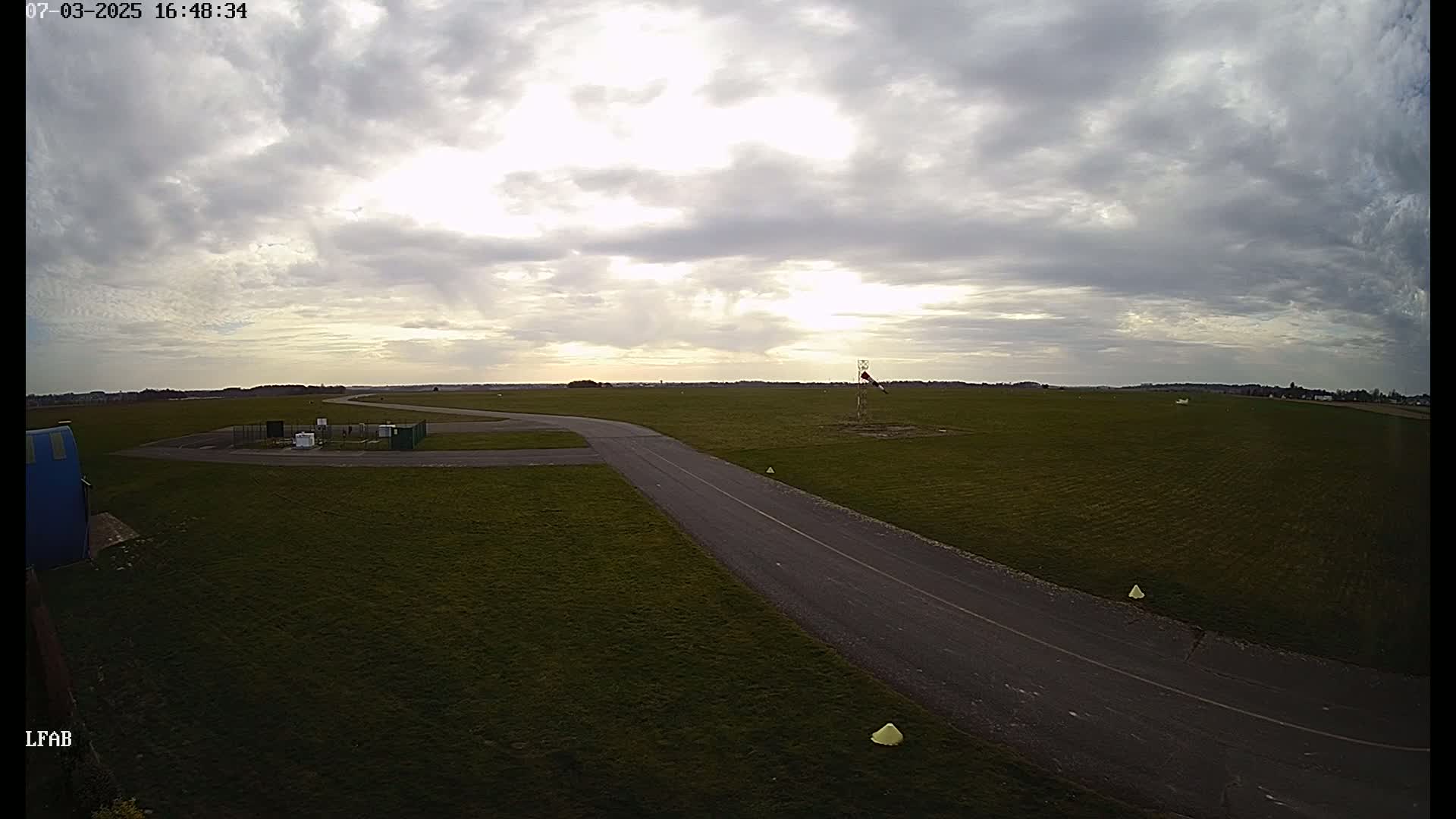 A paved taxiway curves through a grassy airfield under a partly cloudy sky.