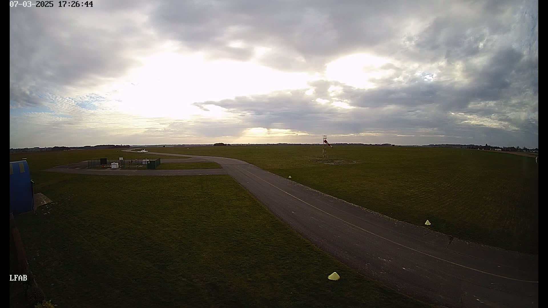 An airfield with a paved taxiway is visible under a partly cloudy sky.